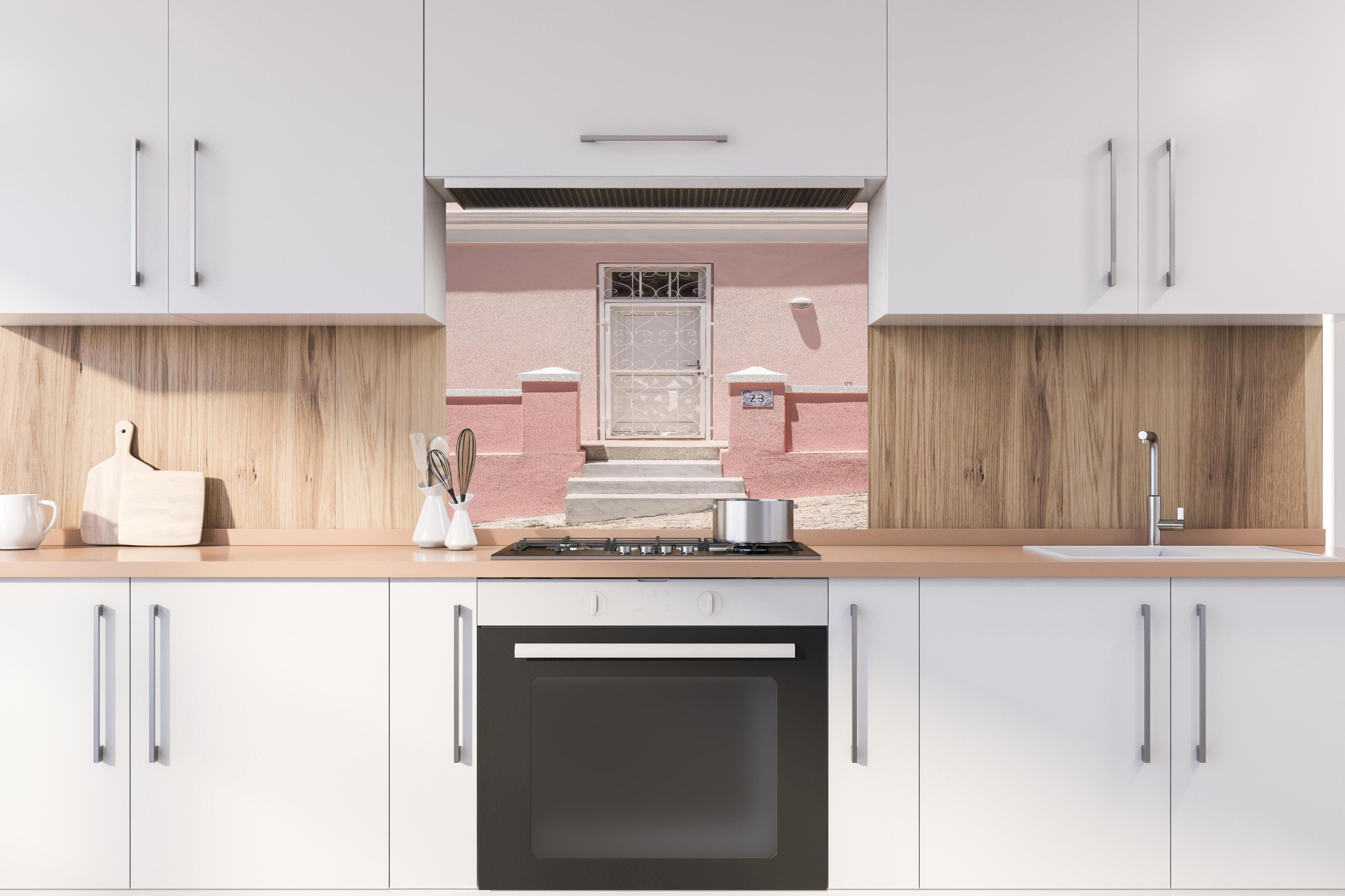 Spritzschutz - Charmante pastellrosa Hausfassade hinter einem Cerankochfeld zwischen Holz-Kochutensilien