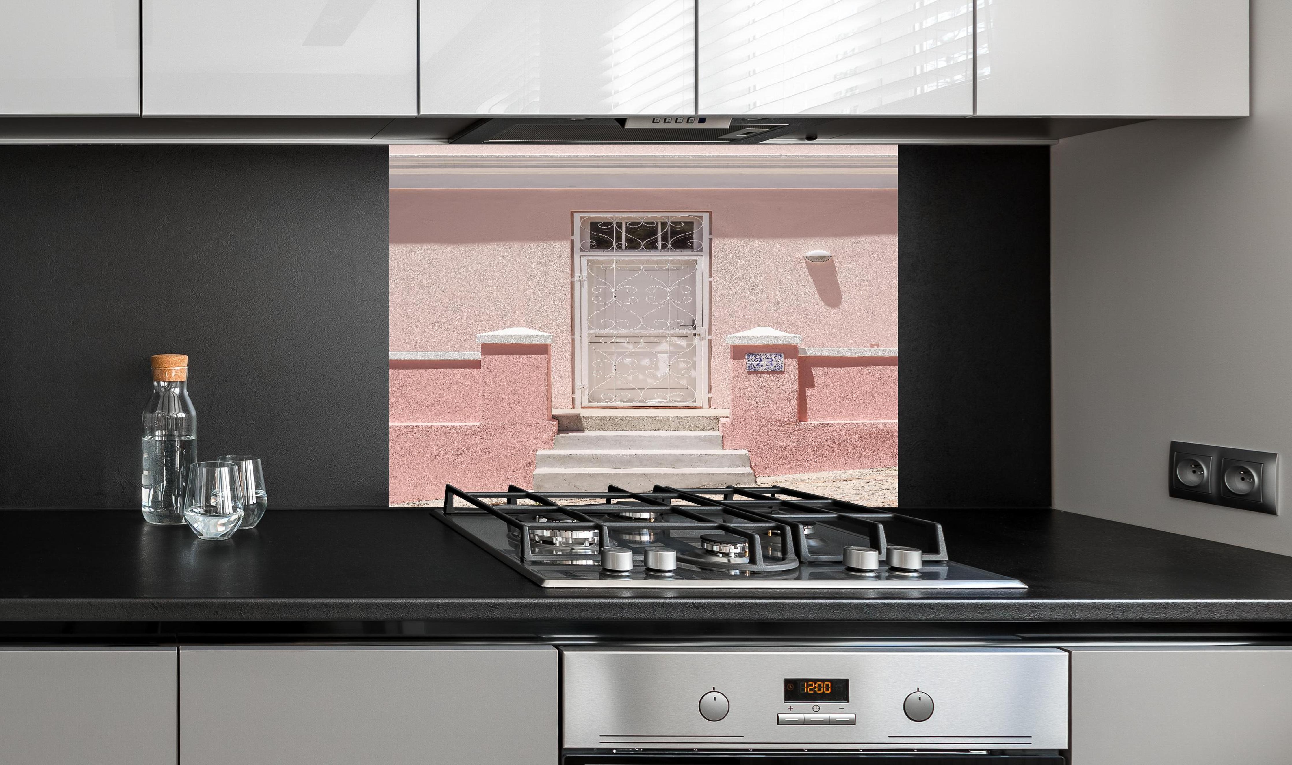 Spritzschutz - Charmante pastellrosa Hausfassade hinter einem Cerankochfeld zwischen Holz-Kochutensilien