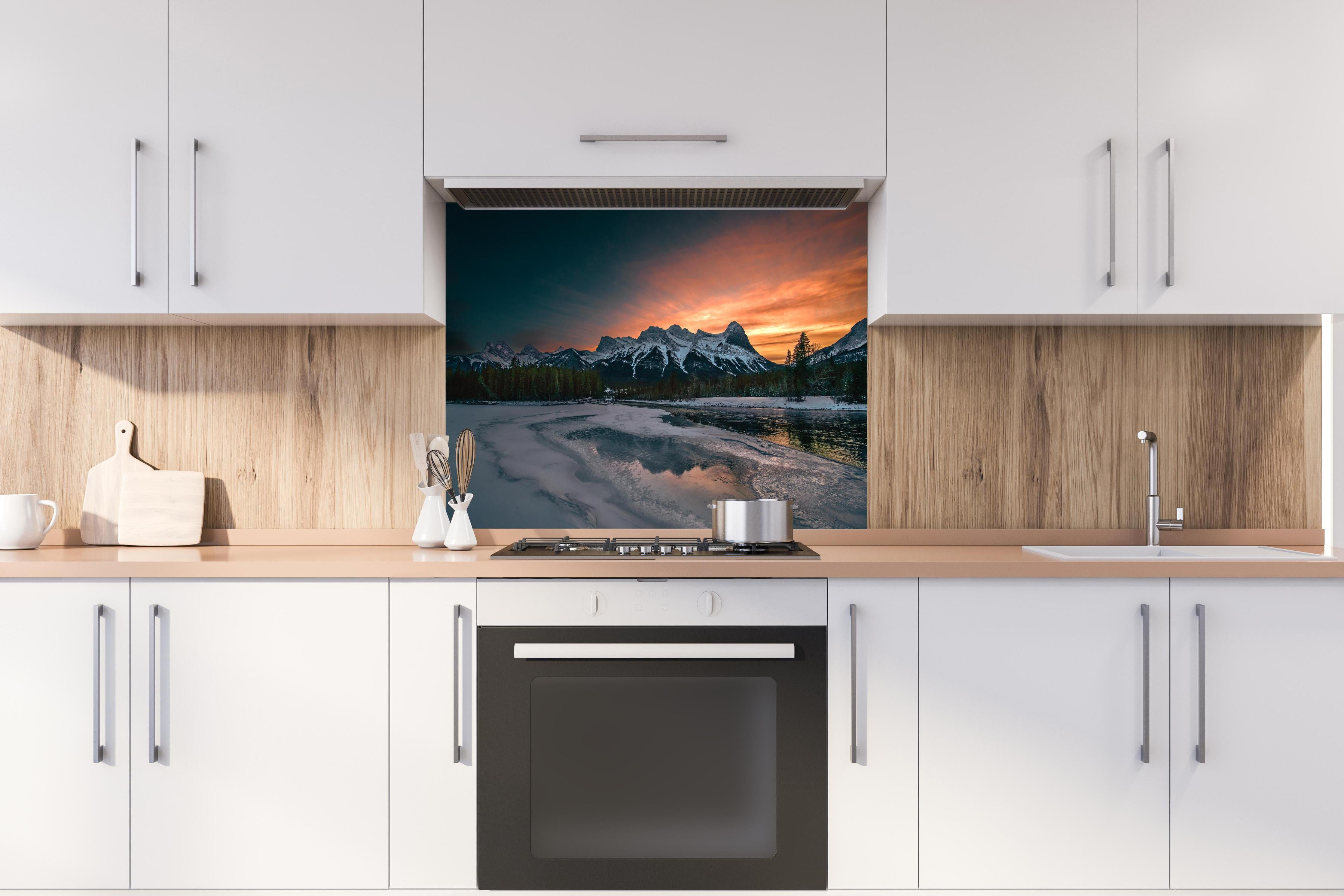 Spritzschutz - Dämmerung über schneebedeckten Bergspitzen hinter einem Cerankochfeld zwischen Holz-Kochutensilien