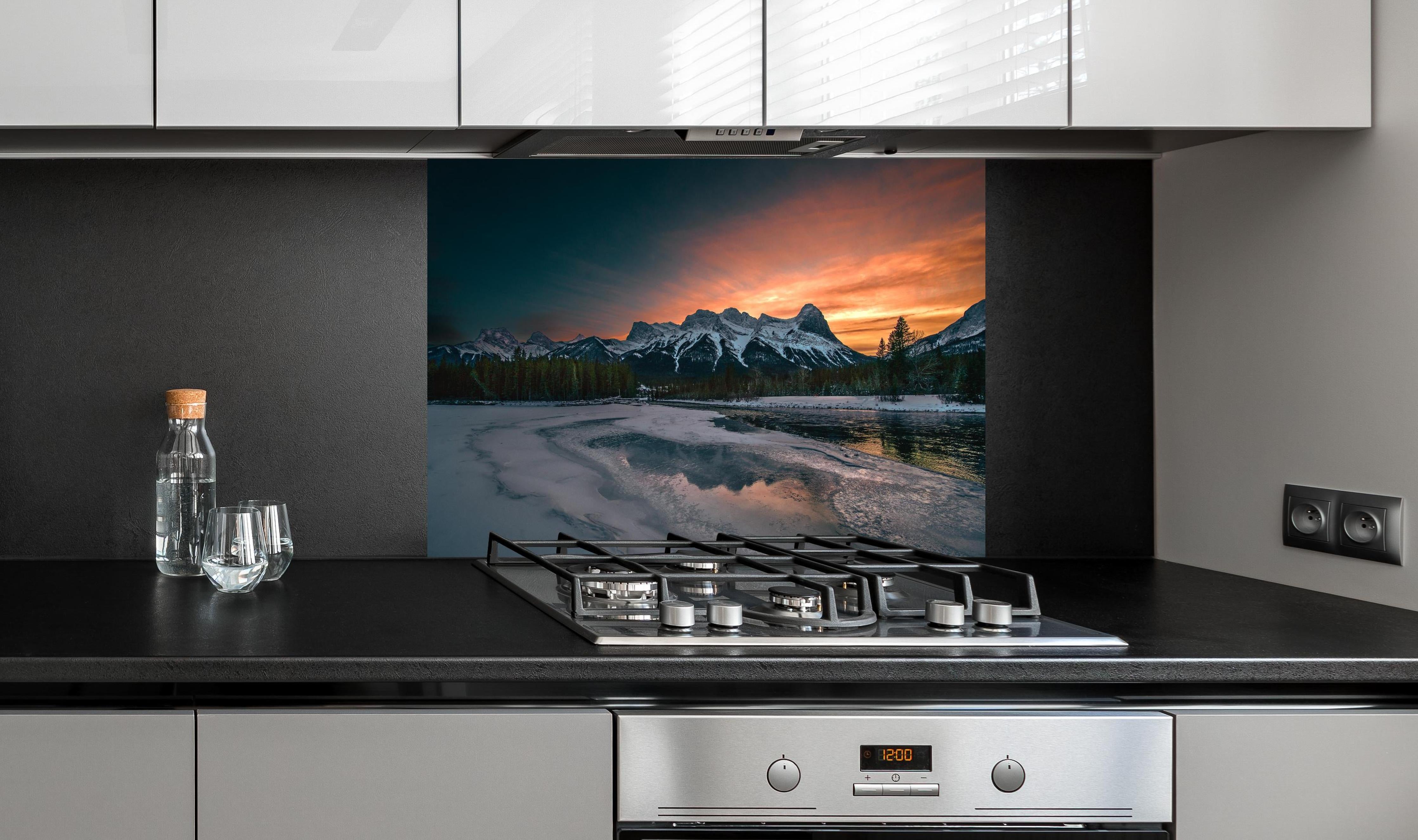 Spritzschutz - Dämmerung über schneebedeckten Bergspitzen hinter einem Cerankochfeld zwischen Holz-Kochutensilien