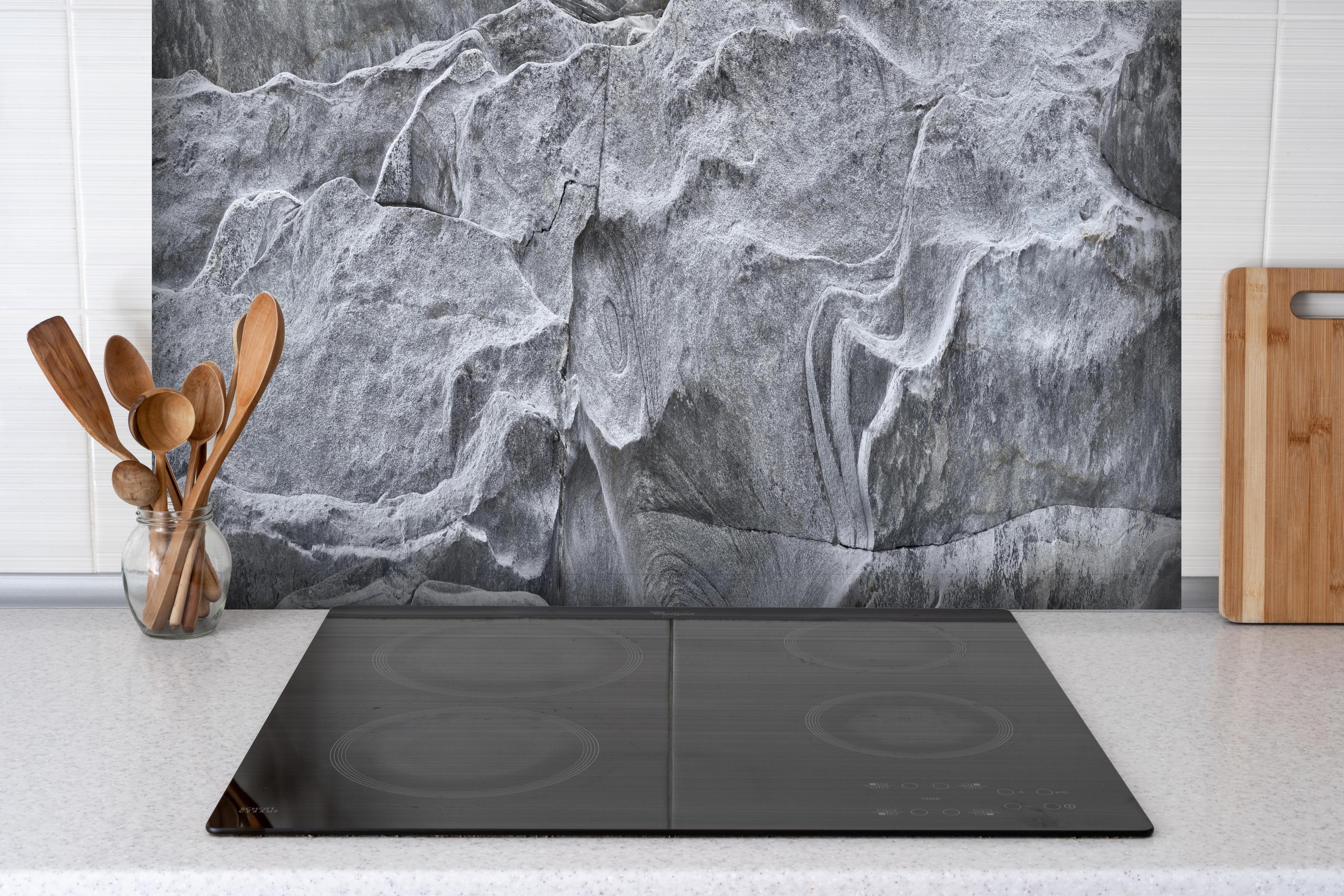 Spritzschutz - Detailaufnahme Grauer Fels Verzasca Fluss hinter einem Cerankochfeld zwischen Holz-Kochutensilien