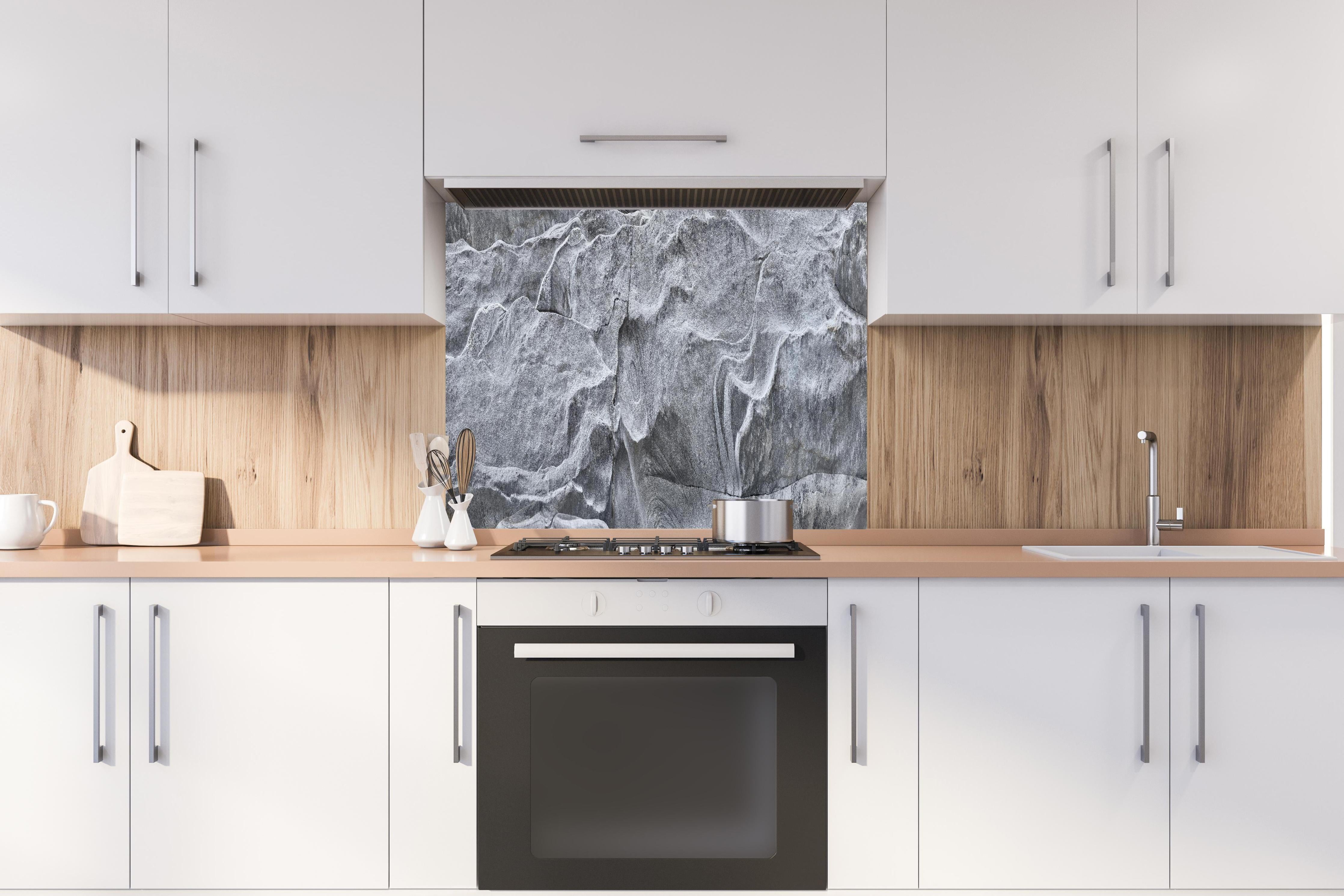 Spritzschutz - Detailaufnahme Grauer Fels Verzasca Fluss hinter einem Cerankochfeld zwischen Holz-Kochutensilien