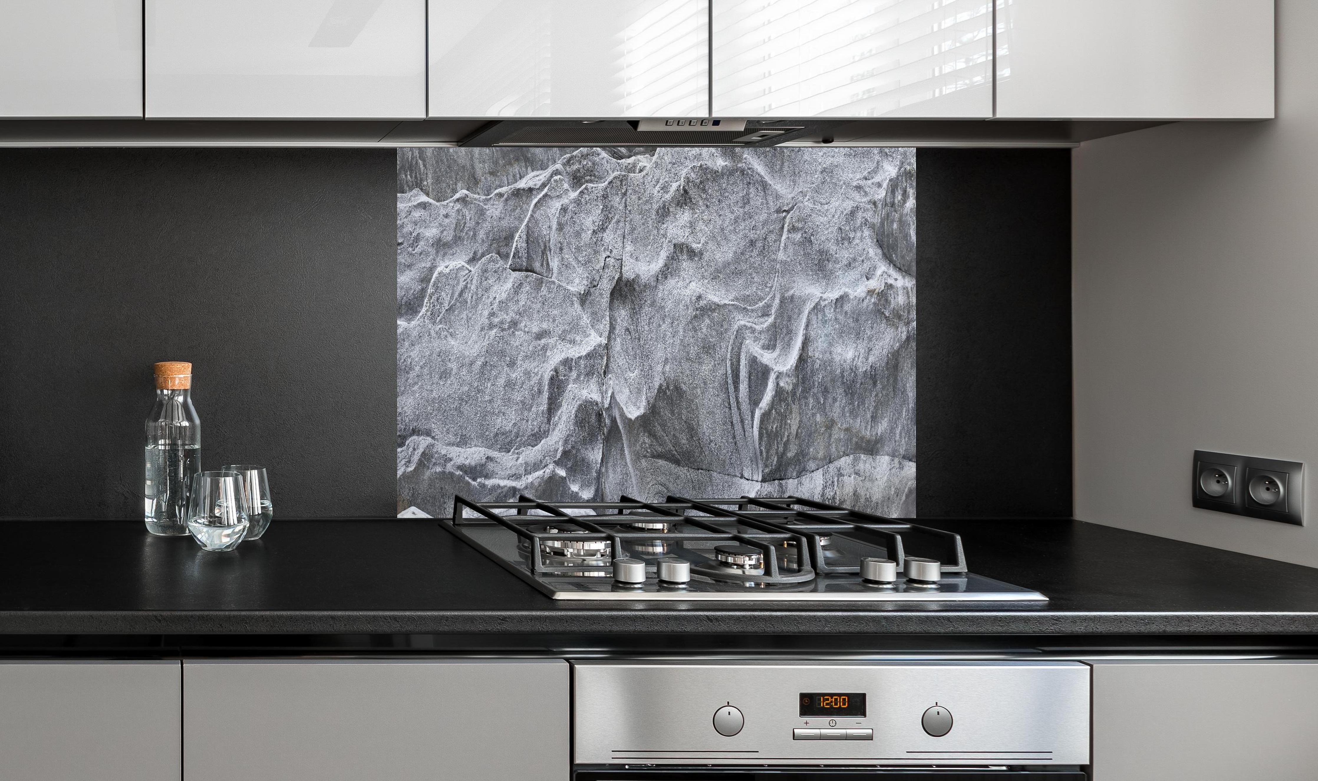 Spritzschutz - Detailaufnahme Grauer Fels Verzasca Fluss hinter einem Cerankochfeld zwischen Holz-Kochutensilien