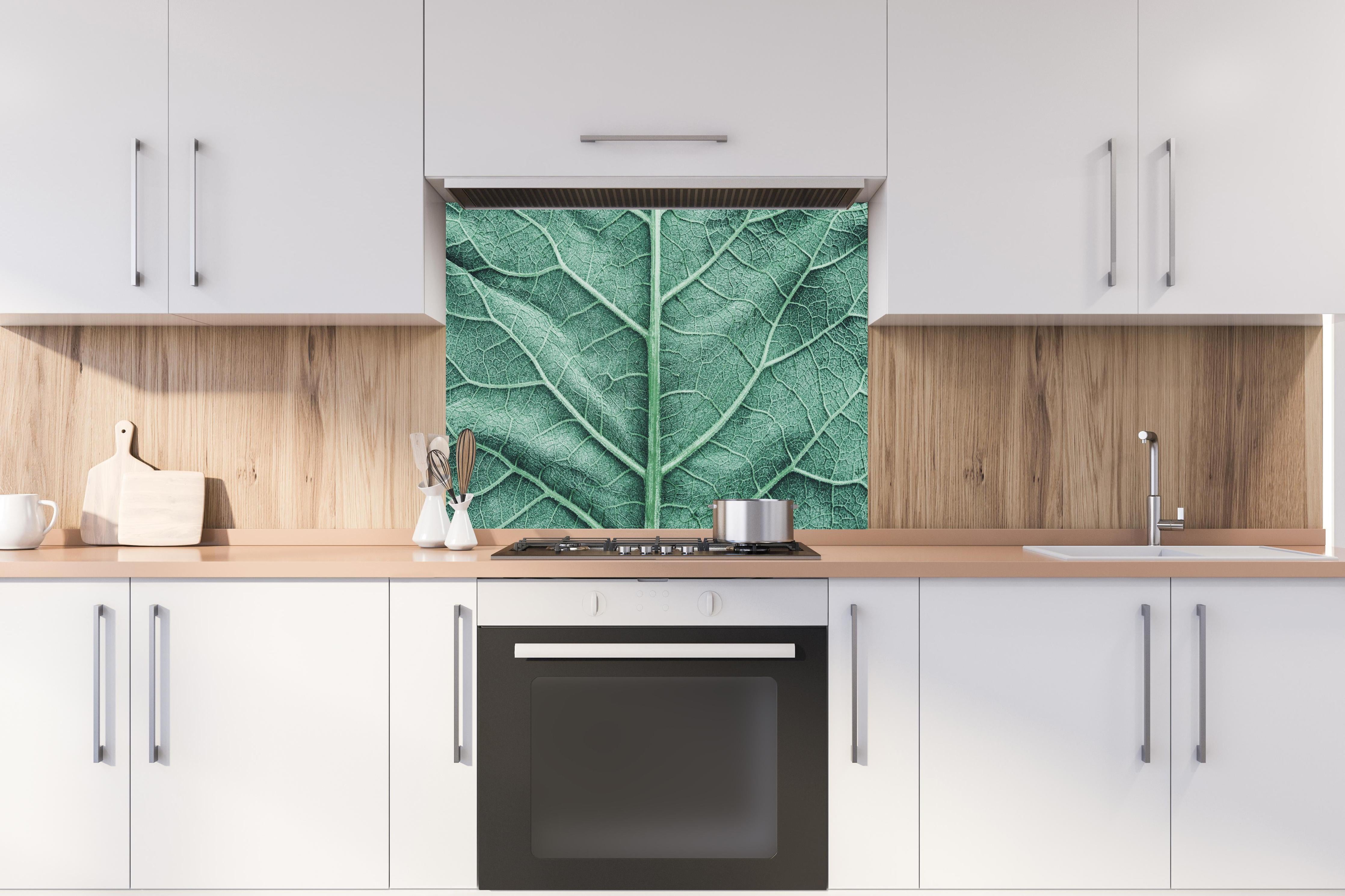 Spritzschutz - Detailreiche grüne Klettenblatt Makroaufnahme hinter einem Cerankochfeld zwischen Holz-Kochutensilien