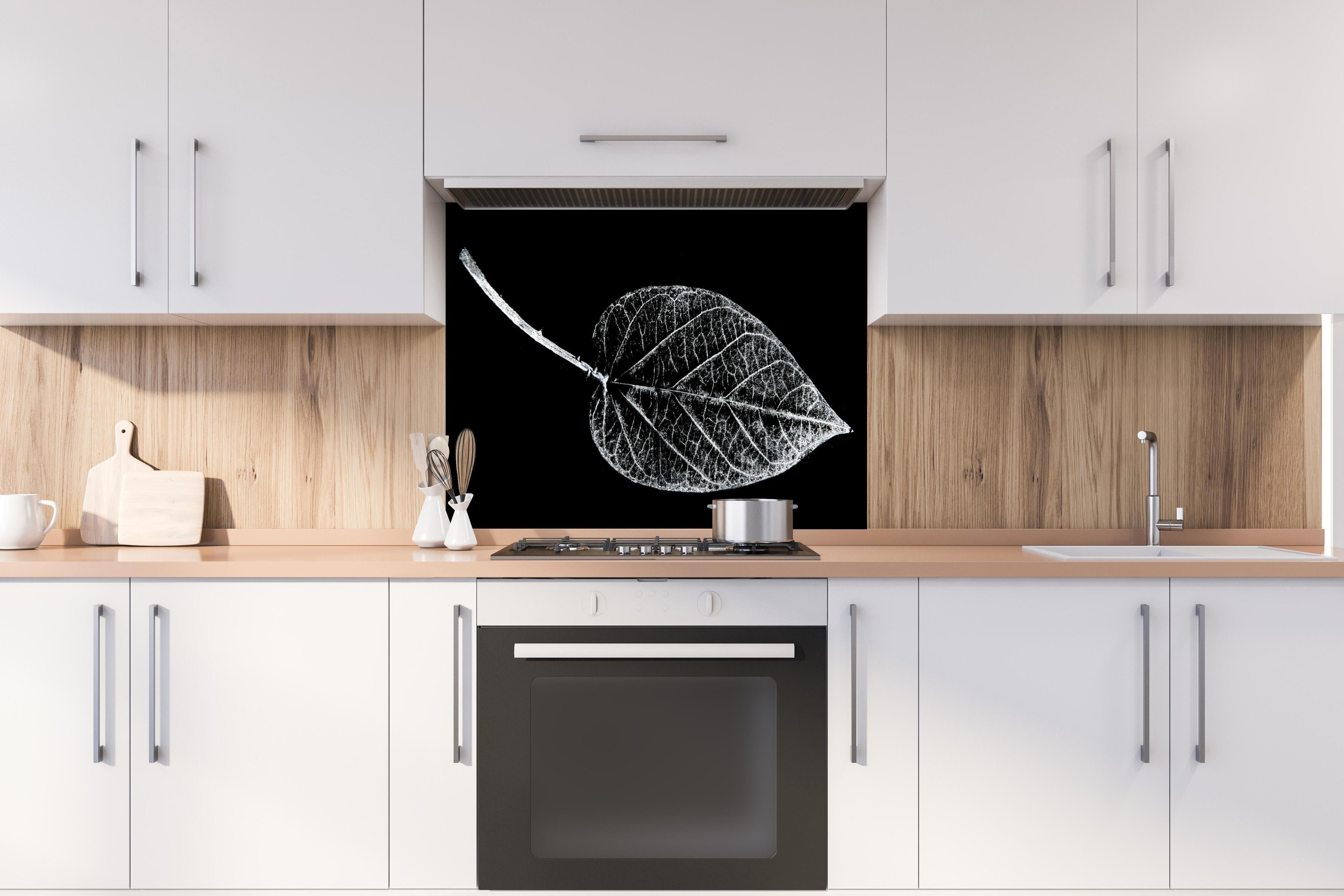 Spritzschutz - Detailreiches Laubblatt in Schwarz und Weiß hinter einem Cerankochfeld zwischen Holz-Kochutensilien