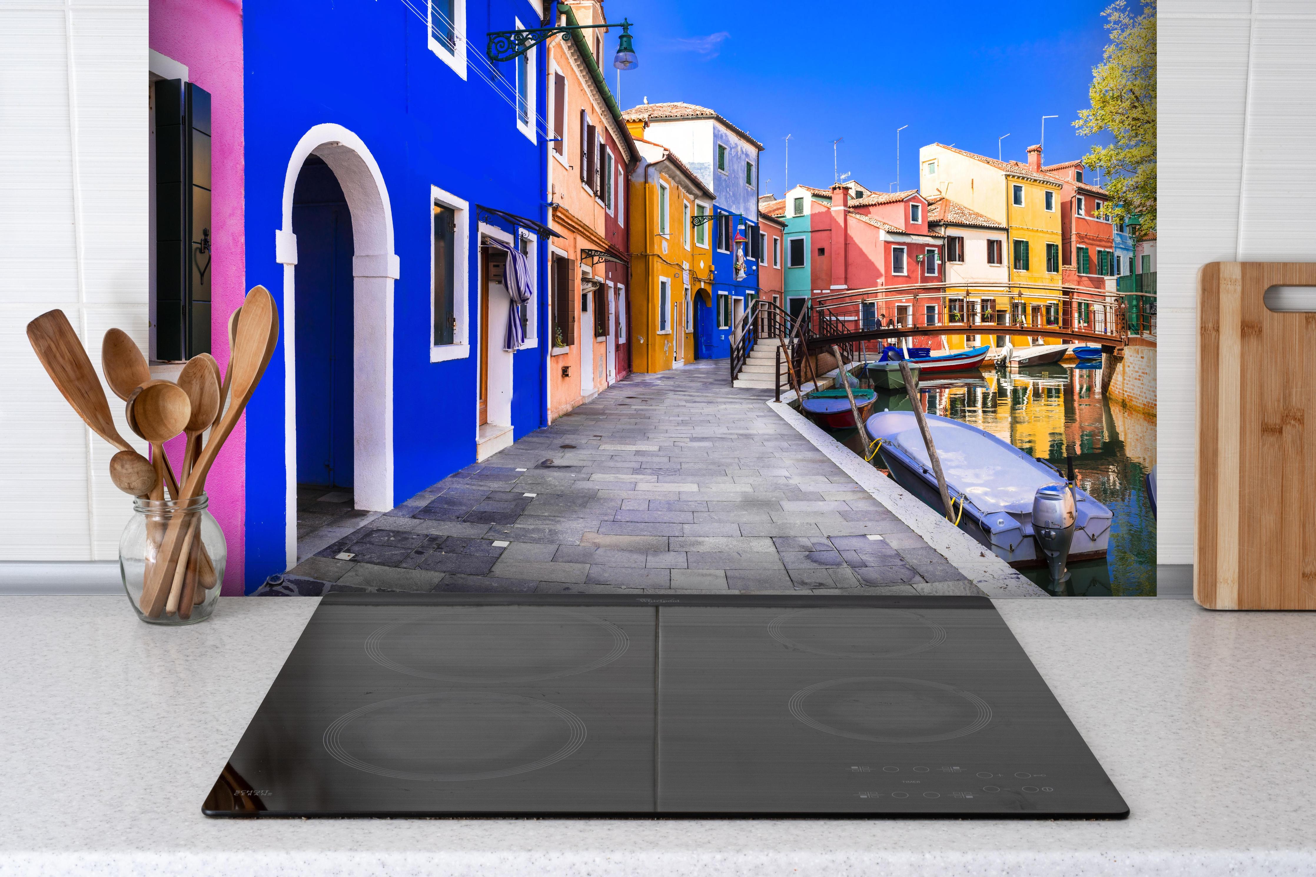 Spritzschutz - Die farbenfrohe Insel Burano hinter einem Cerankochfeld zwischen Holz-Kochutensilien