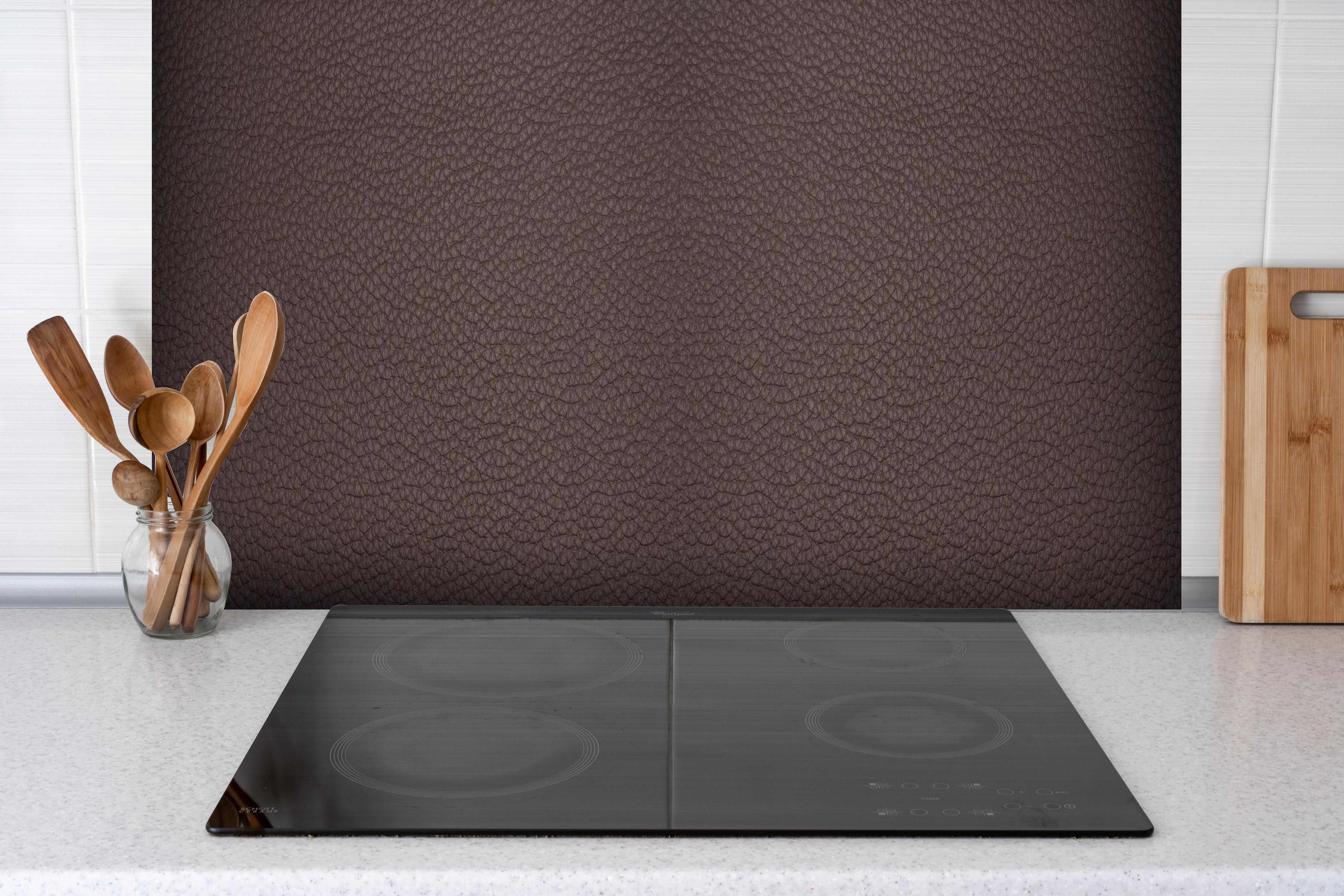Spritzschutz - Dunkelbraune Lederstruktur im Panorama hinter einem Cerankochfeld zwischen Holz-Kochutensilien