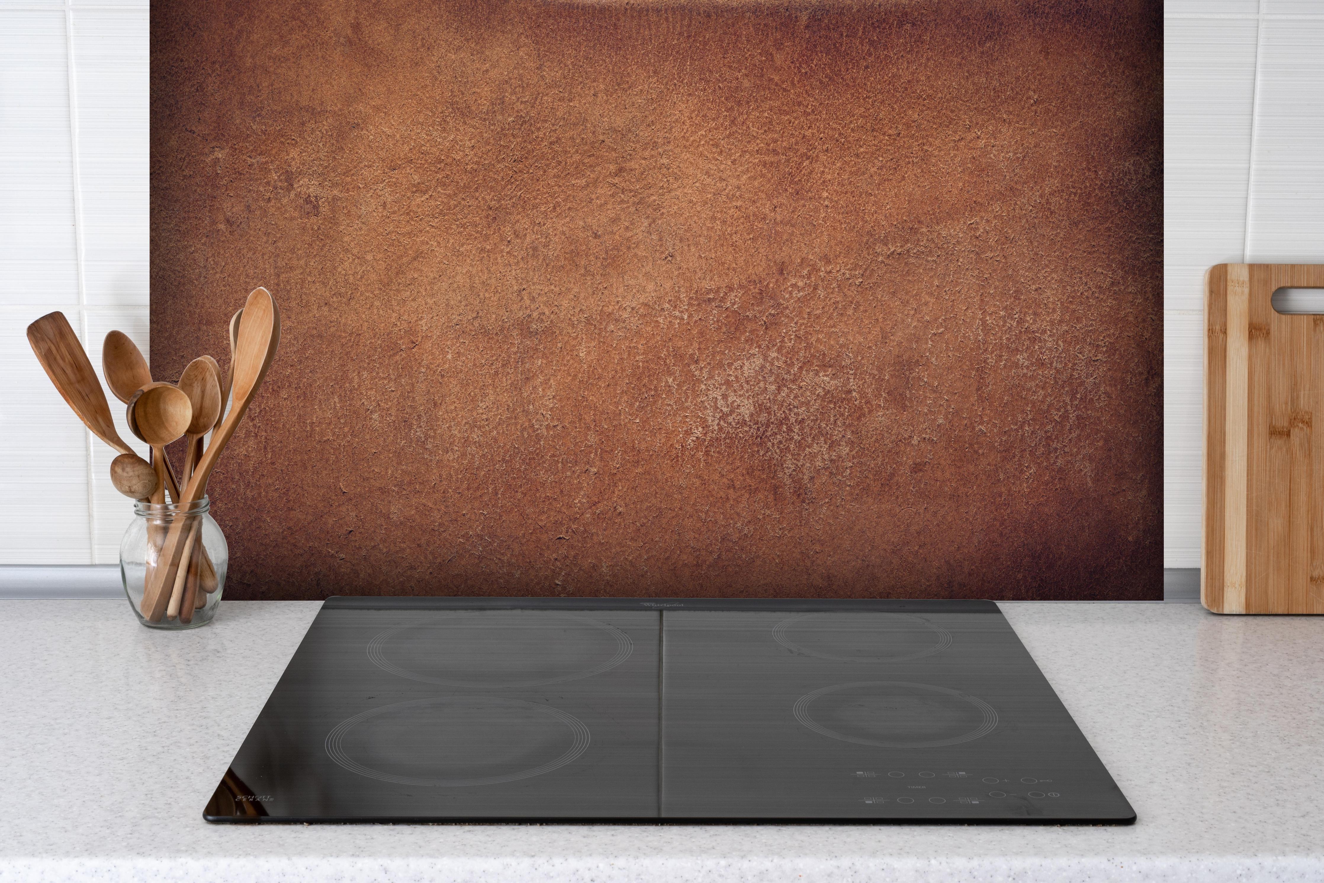 Spritzschutz - Dunkelbraune Ledertextur hinter einem Cerankochfeld zwischen Holz-Kochutensilien