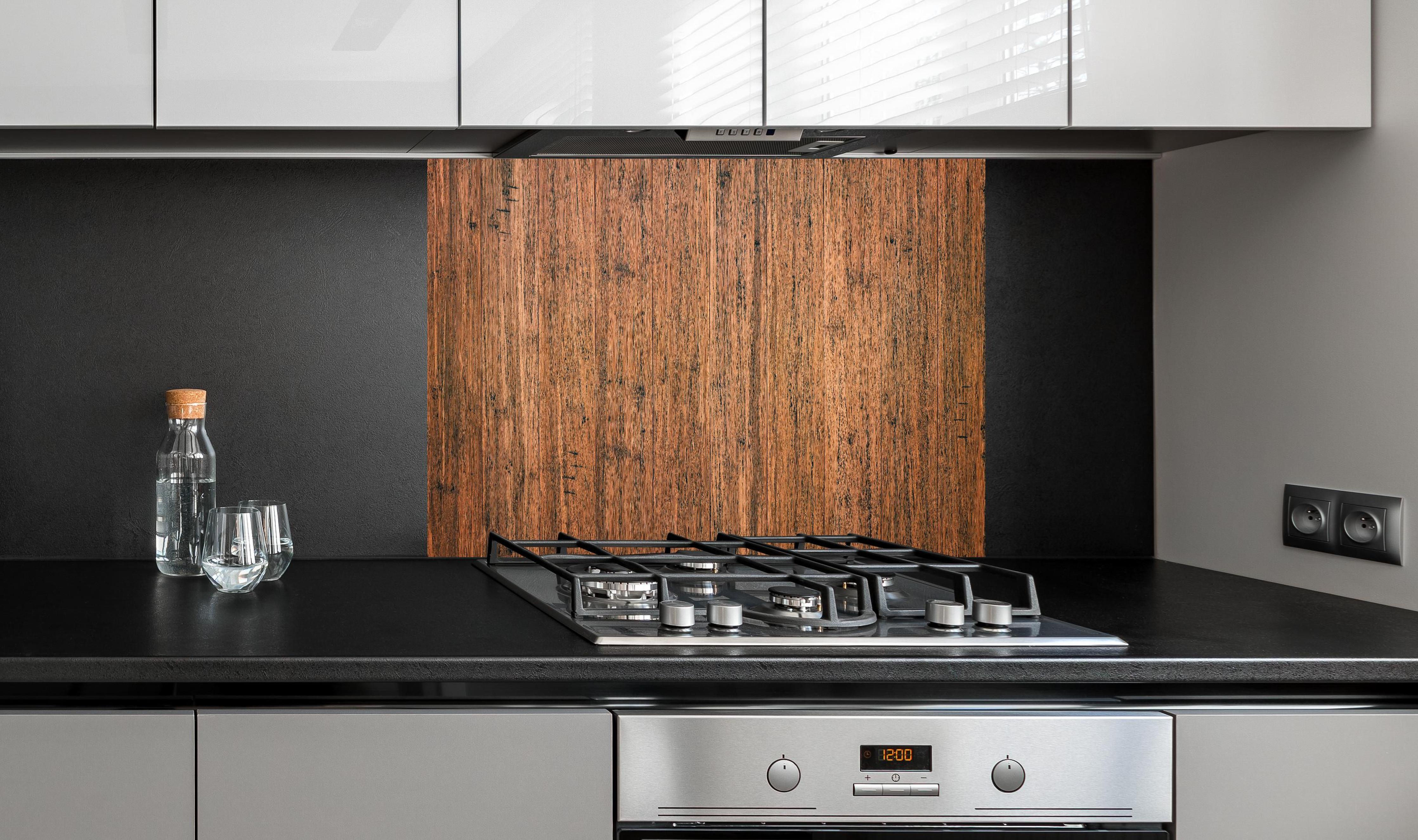 Spritzschutz - Dunkelbraunes rustikales Holzbrett hinter einem Cerankochfeld zwischen Holz-Kochutensilien