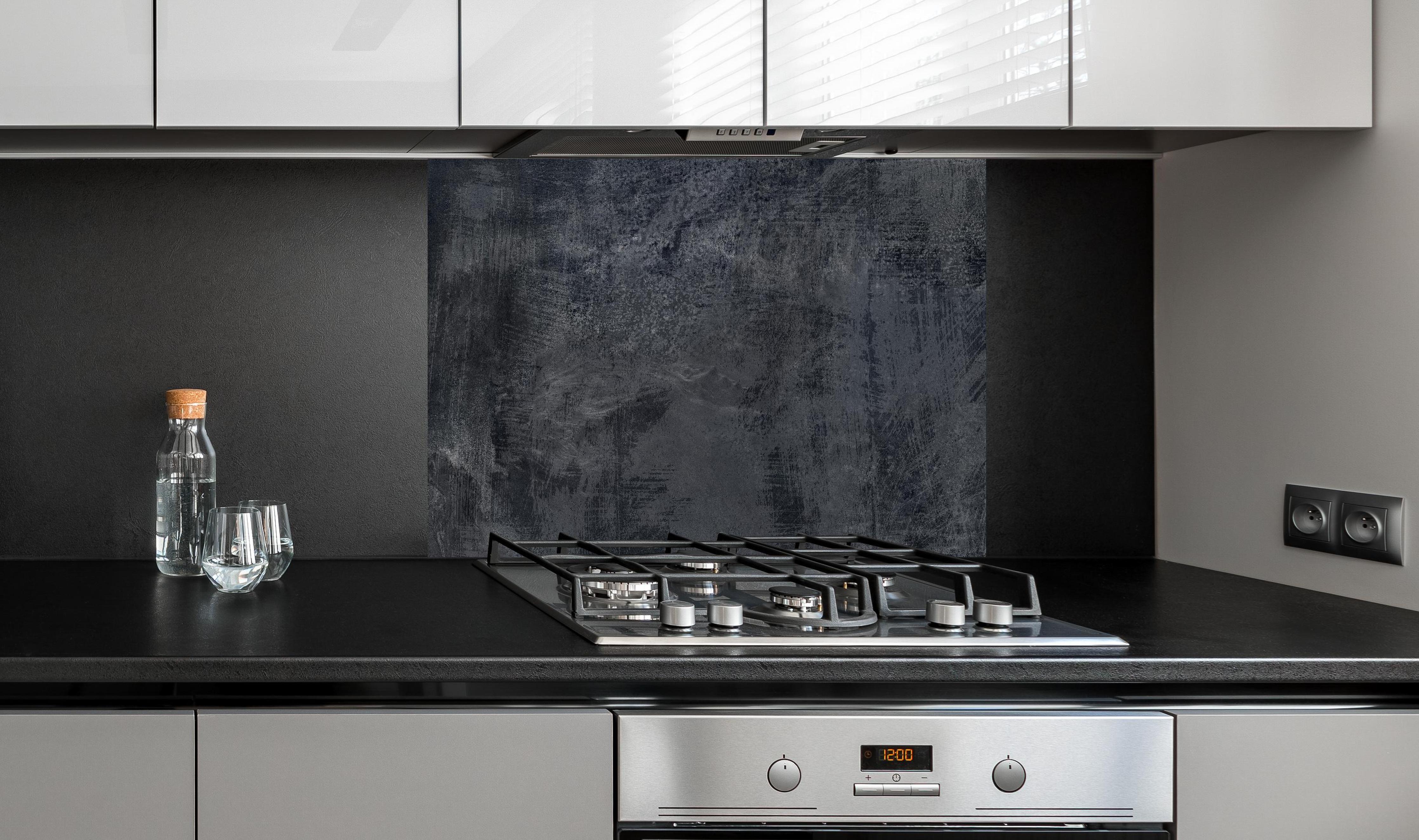 Spritzschutz - Dunkelgrauer Zement-Hintergrund hinter einem Cerankochfeld zwischen Holz-Kochutensilien