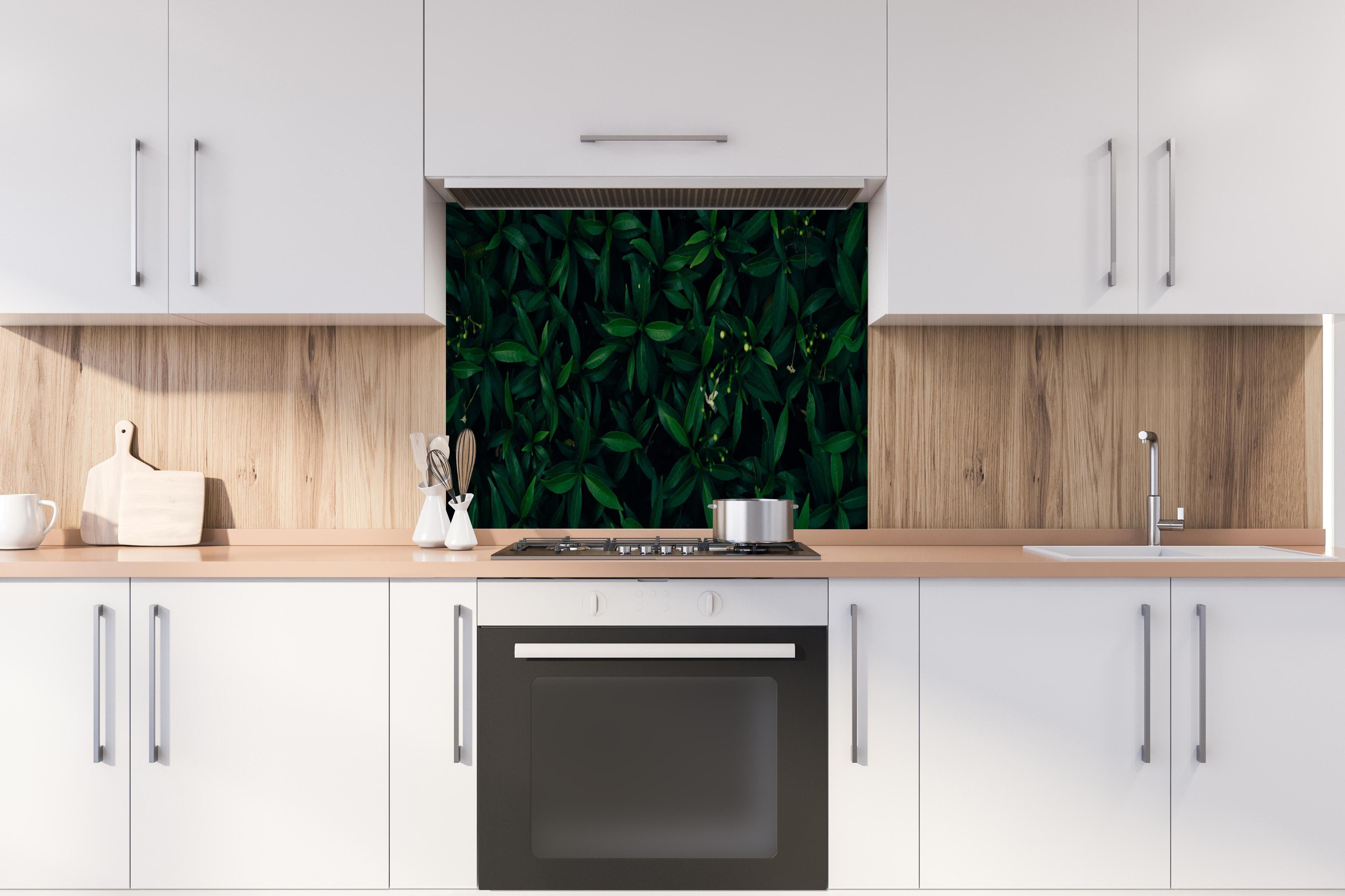 Spritzschutz - Dunkelgrüne Blätter dezentes Naturmuster hinter einem Cerankochfeld zwischen Holz-Kochutensilien