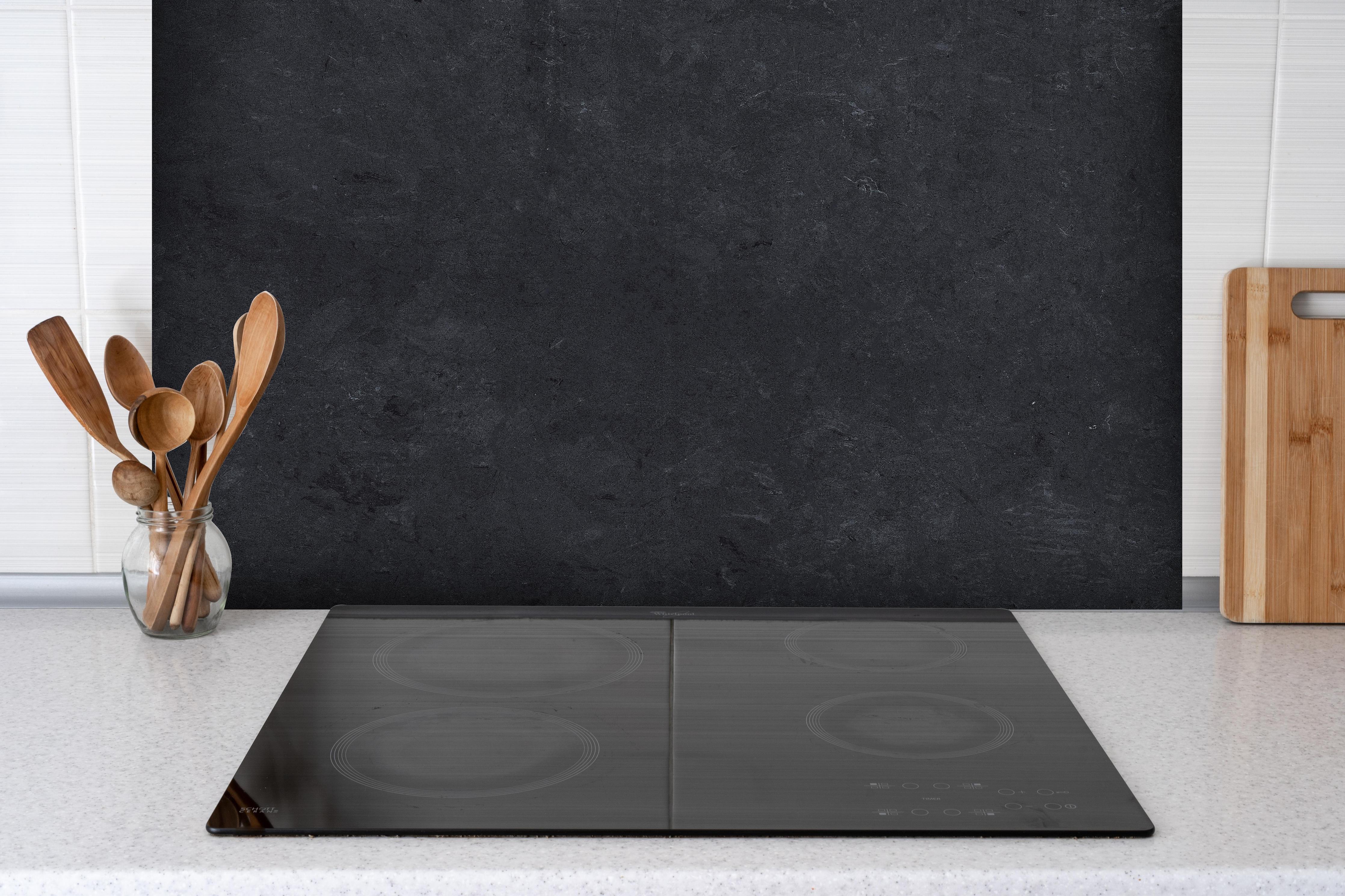 Spritzschutz - Dunkle Stein- oder Schieferwand hinter einem Cerankochfeld zwischen Holz-Kochutensilien