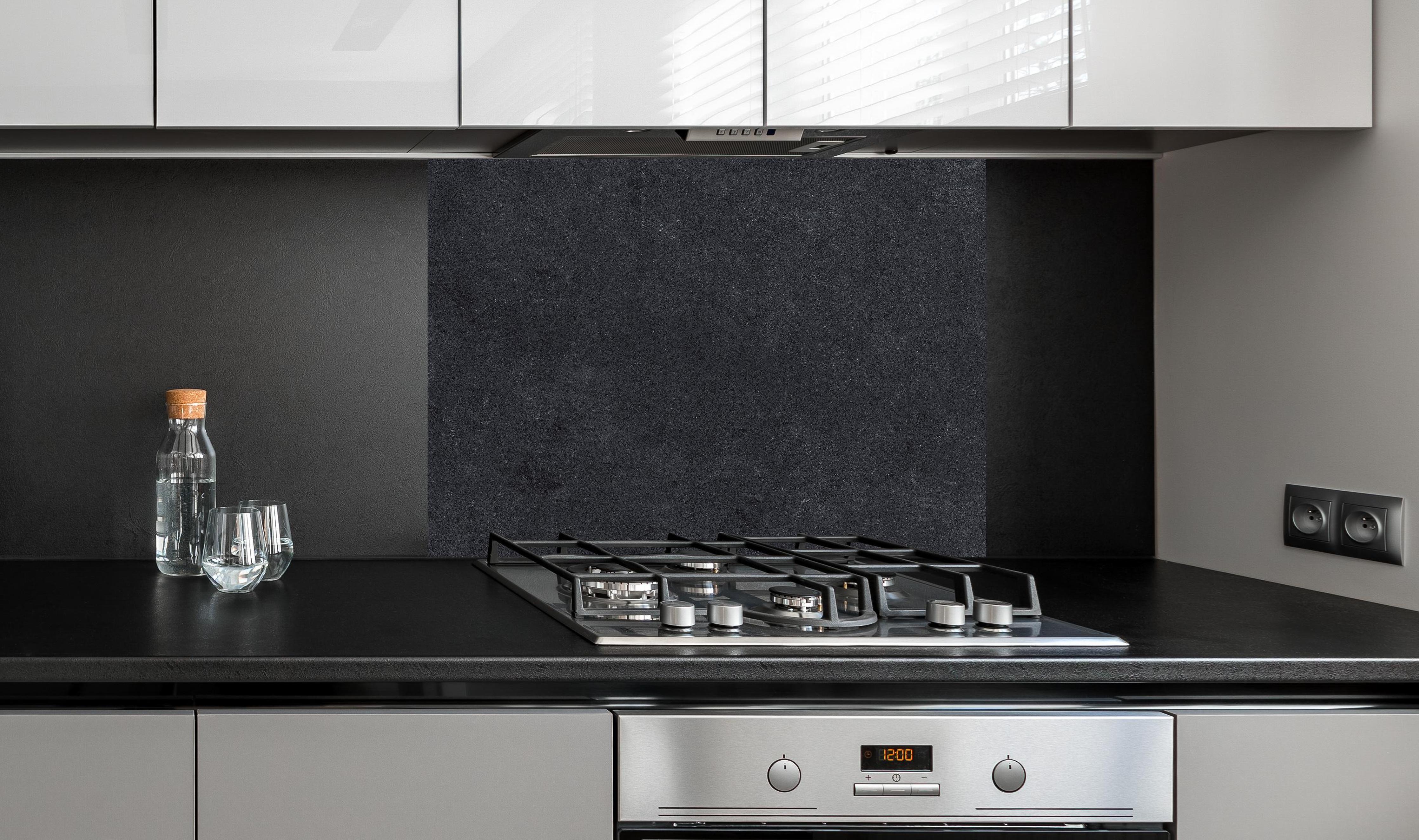 Spritzschutz - Dunkle Stein- oder Schieferwand hinter einem Cerankochfeld zwischen Holz-Kochutensilien