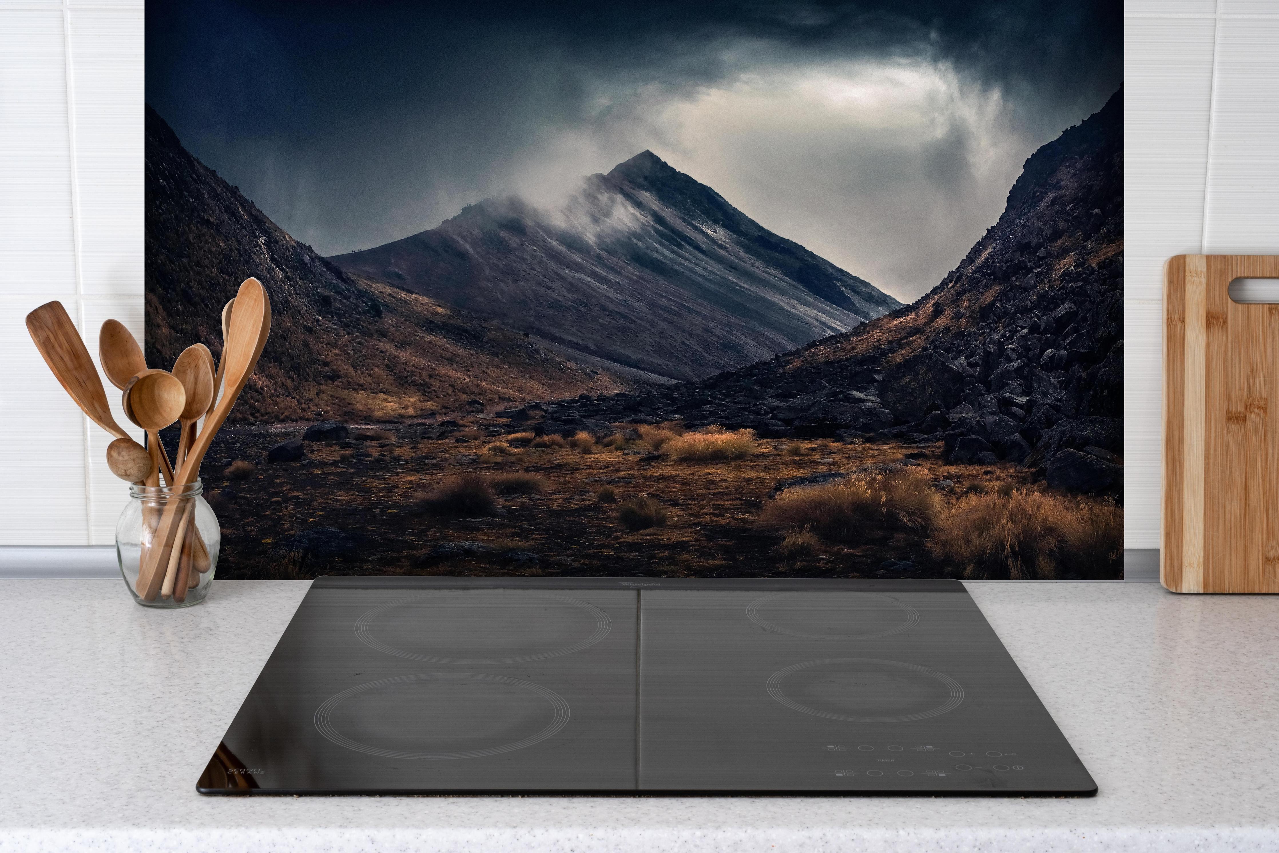 Spritzschutz - Dunkle Wolken Aufziehend über Bergspitze hinter einem Cerankochfeld zwischen Holz-Kochutensilien