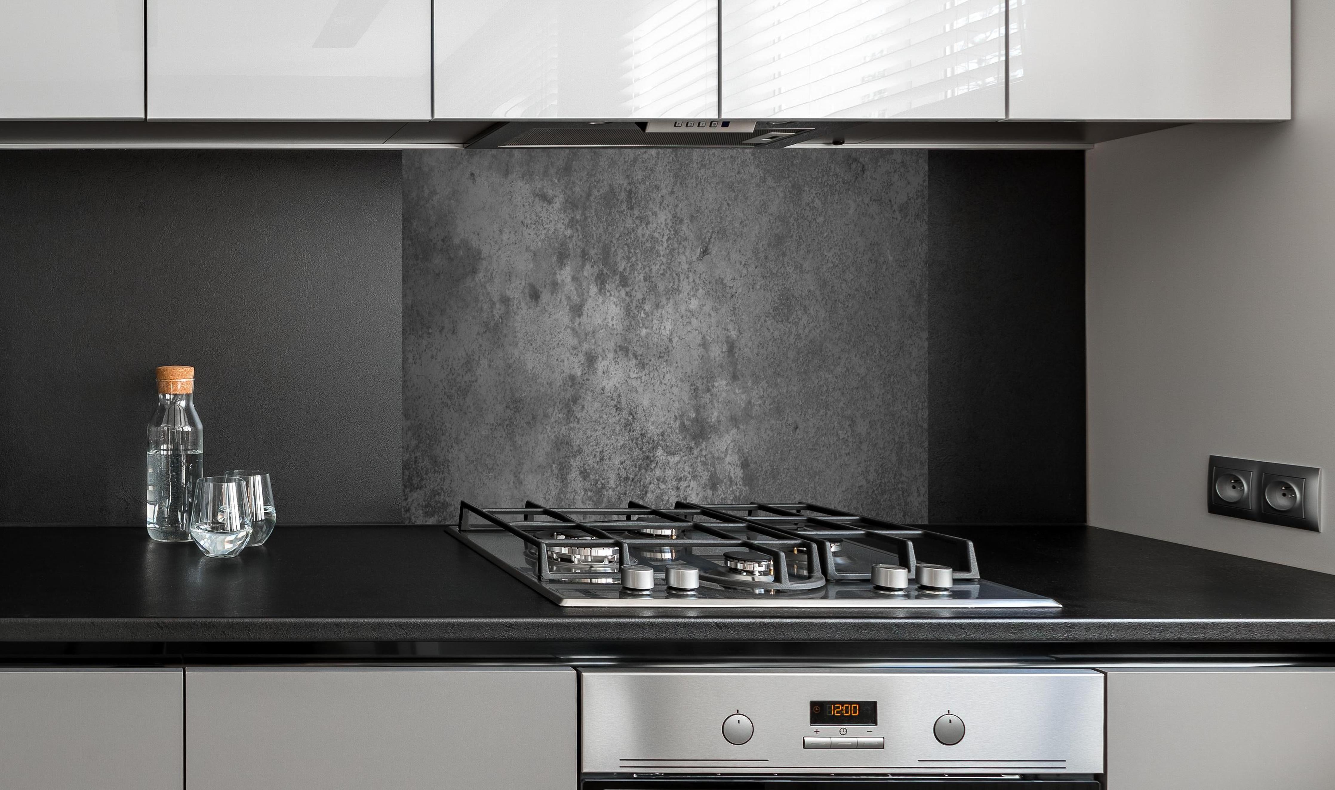 Spritzschutz - Dunkle alte Zementwand hinter einem Cerankochfeld zwischen Holz-Kochutensilien