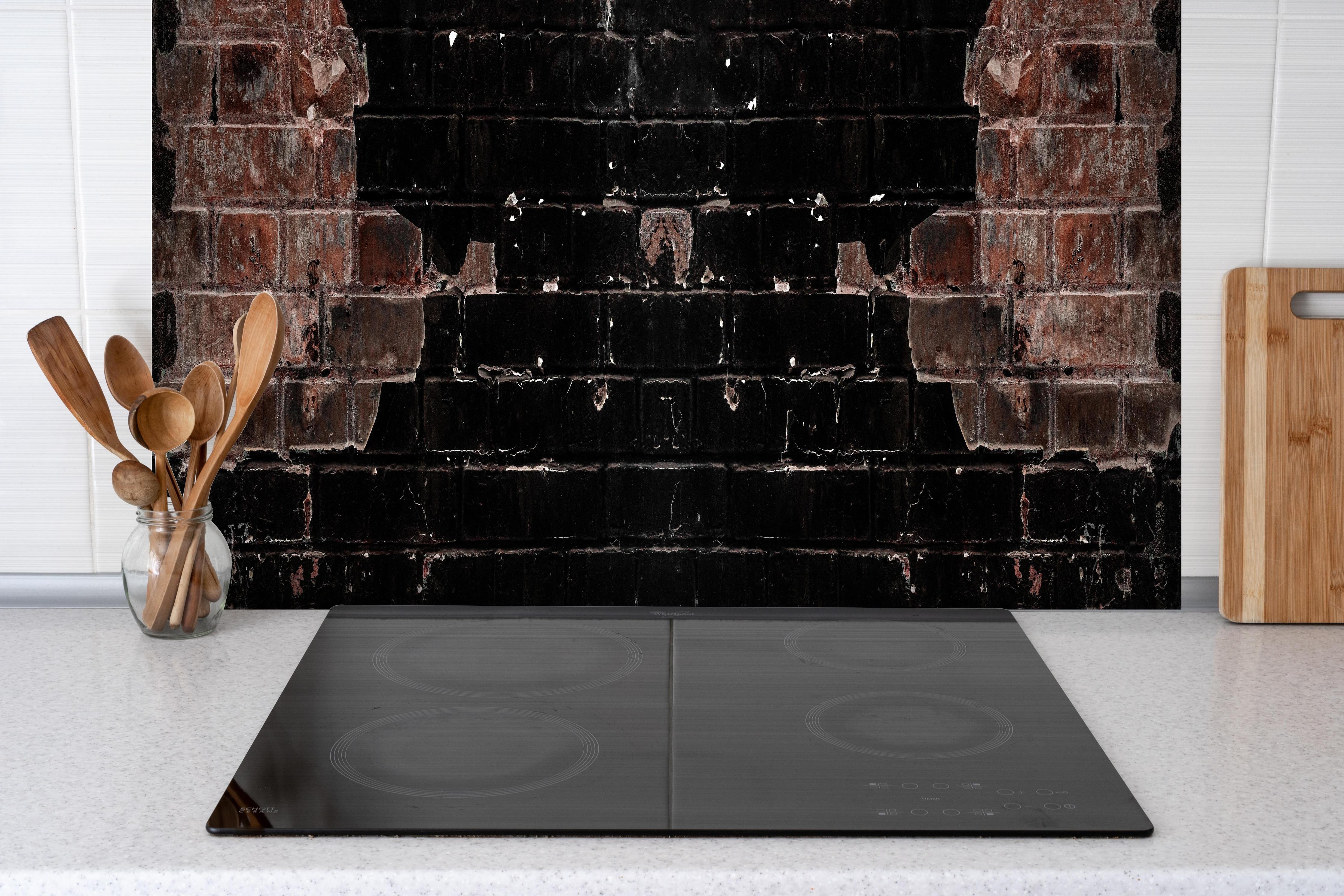 Spritzschutz - Dunkle beschädigte Ziegelwand hinter einem Cerankochfeld zwischen Holz-Kochutensilien