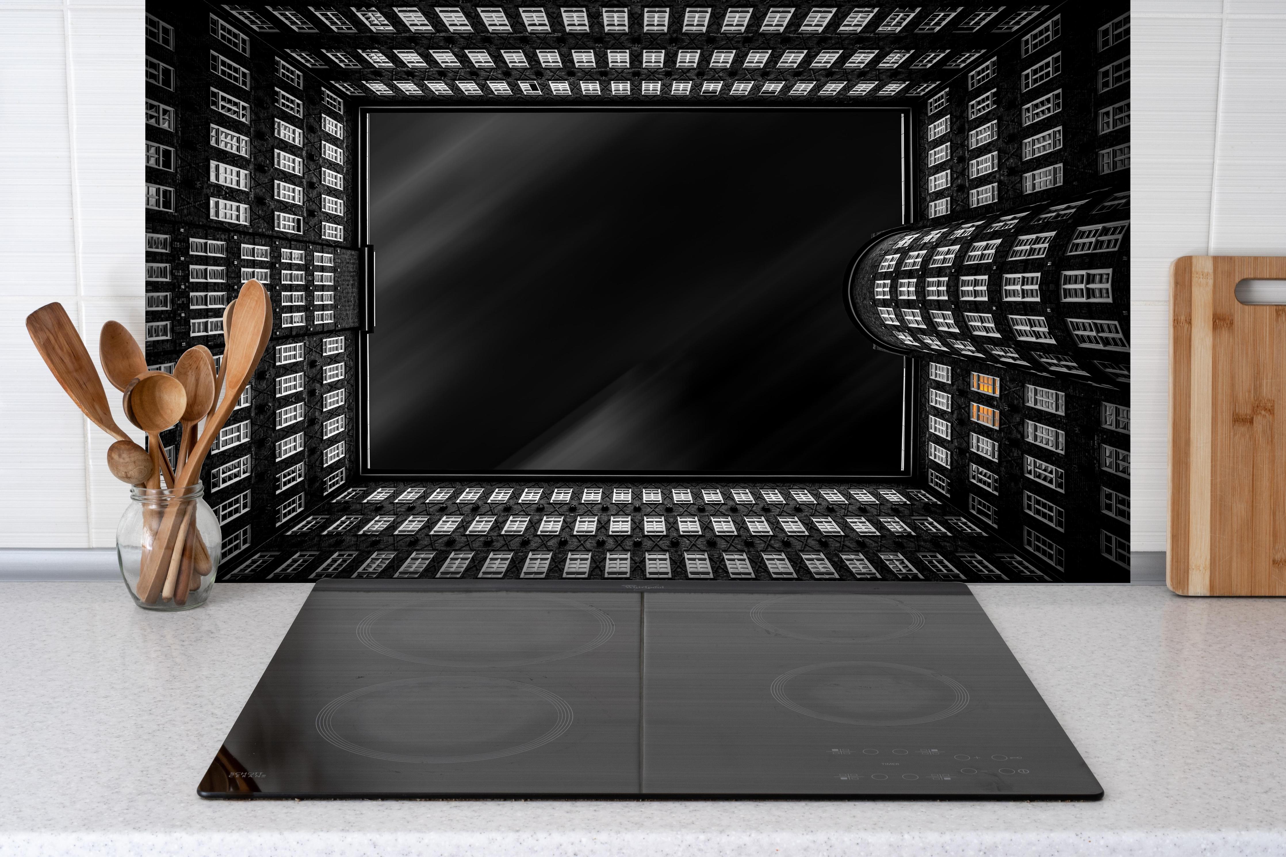 Spritzschutz - Dunkles Gebäude bei Nacht hinter einem Cerankochfeld zwischen Holz-Kochutensilien