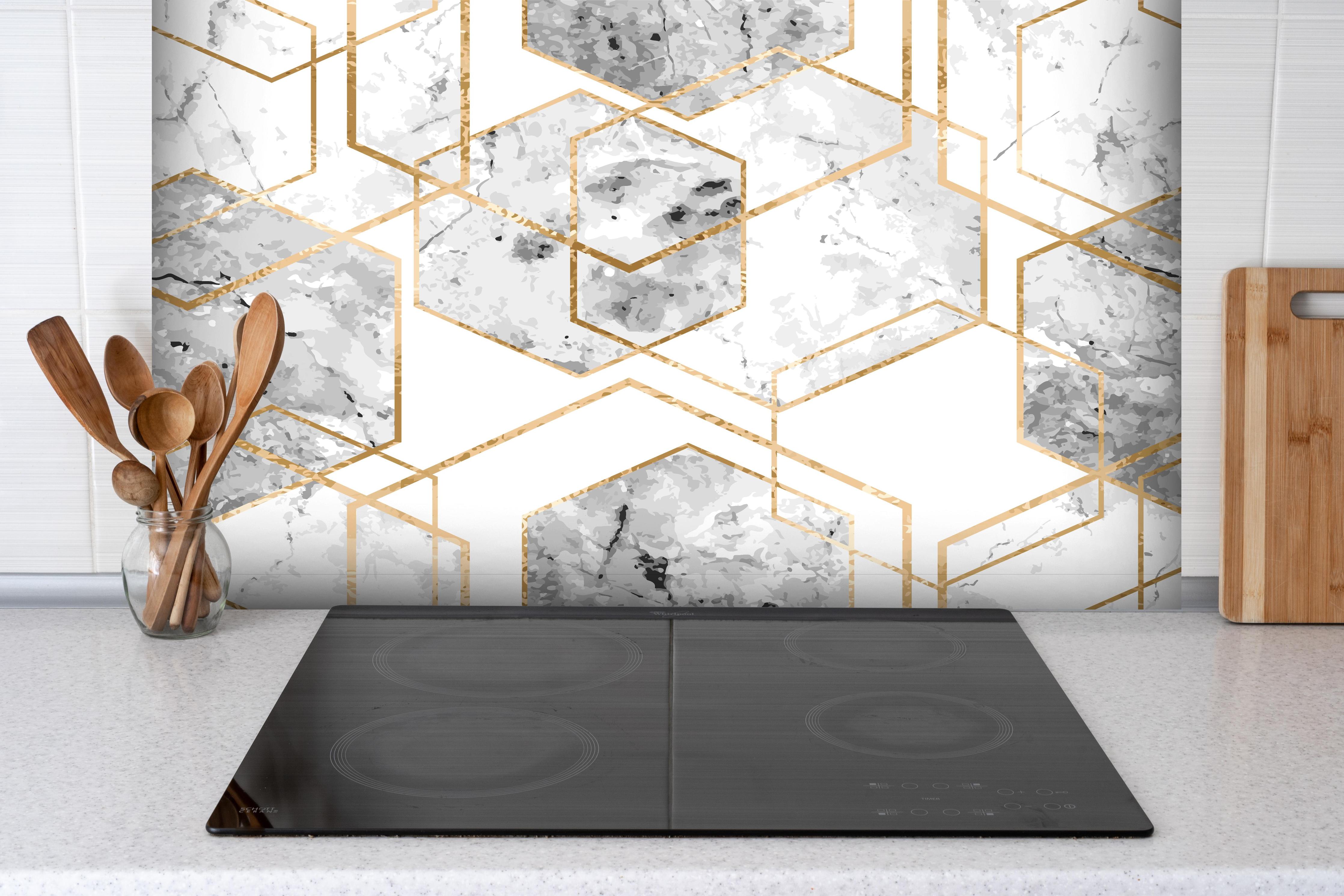 Spritzschutz - Edle Marmoroptik in Weiß und Gold hinter einem Cerankochfeld zwischen Holz-Kochutensilien