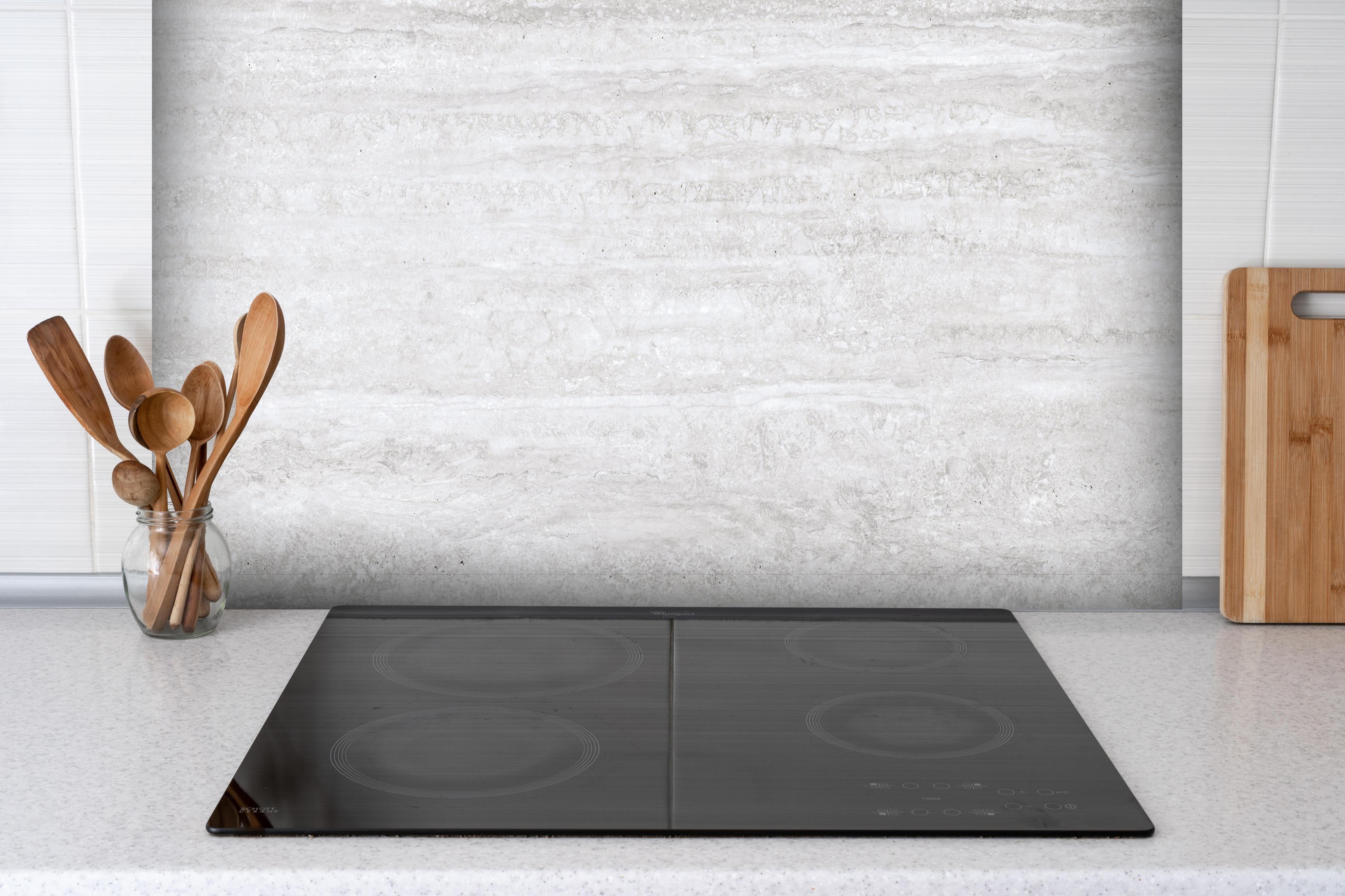 Spritzschutz - Edler Kalksteinmarmor hinter einem Cerankochfeld zwischen Holz-Kochutensilien