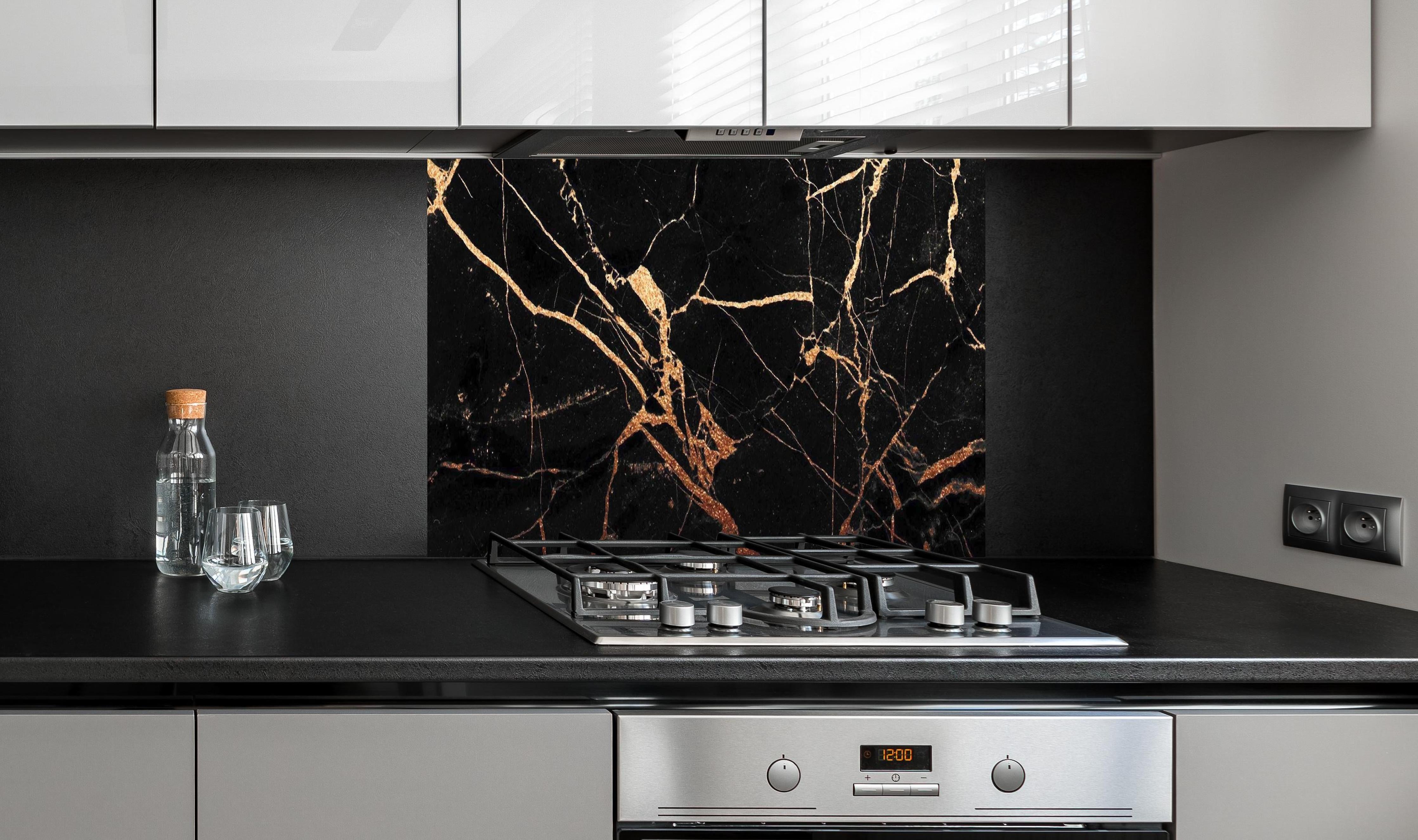 Spritzschutz - Edler Schwarz-Gold Marmor-Optik hinter einem Cerankochfeld zwischen Holz-Kochutensilien