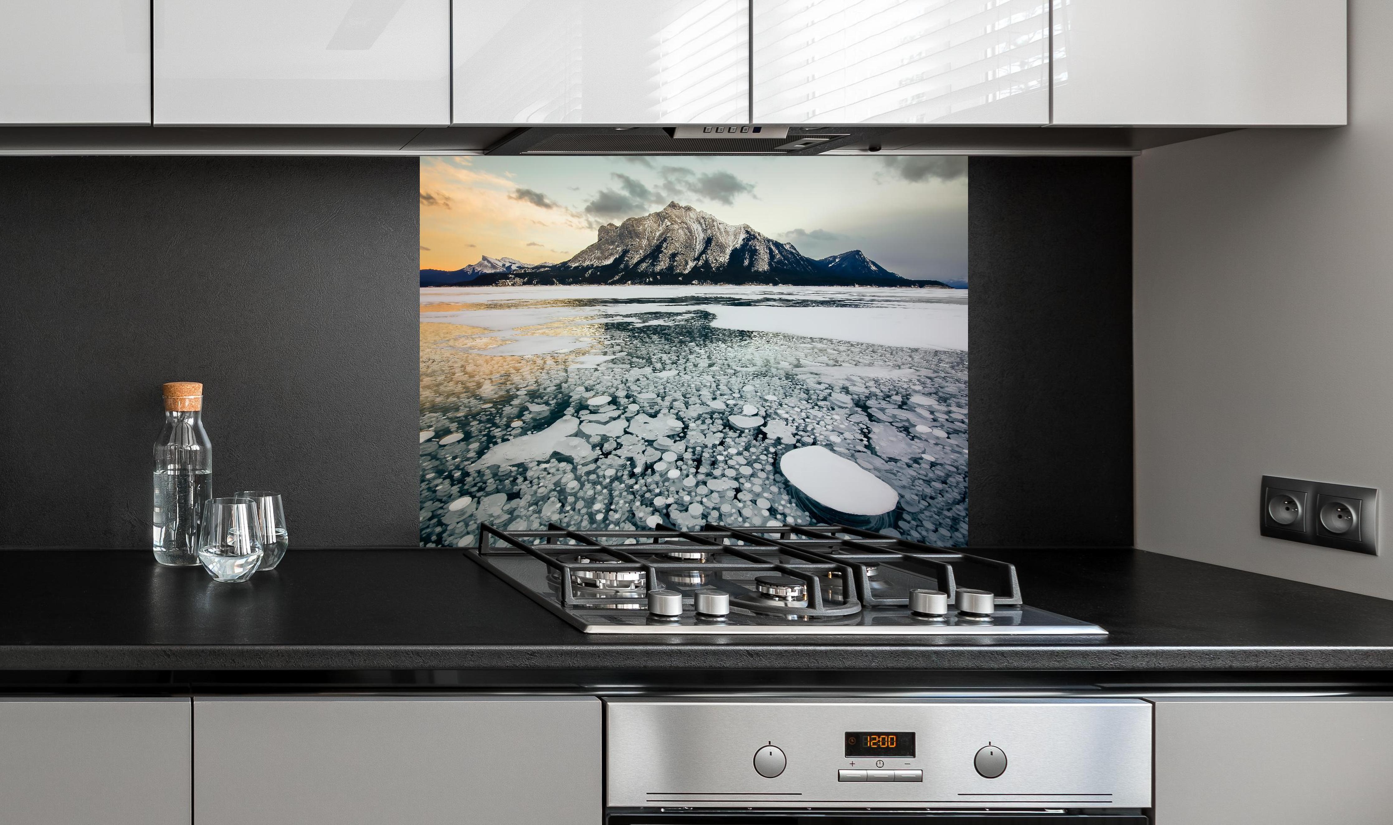 Spritzschutz - Eisblasen im gefrorenen Bergsee bei Sonnenuntergang hinter einem Cerankochfeld zwischen Holz-Kochutensilien