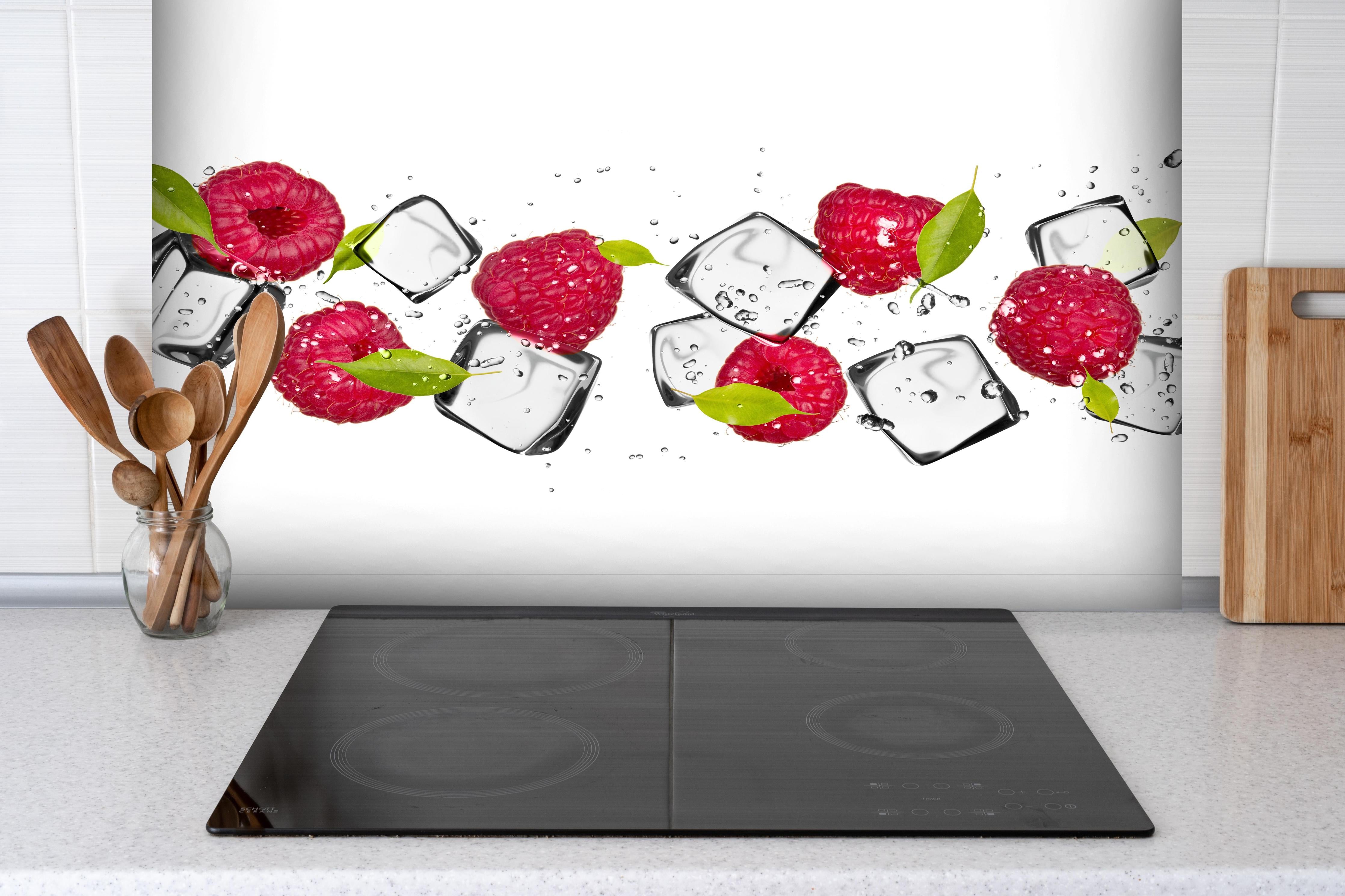 Spritzschutz - Eiswürfel mit Himbeeren hinter einem Cerankochfeld zwischen Holz-Kochutensilien