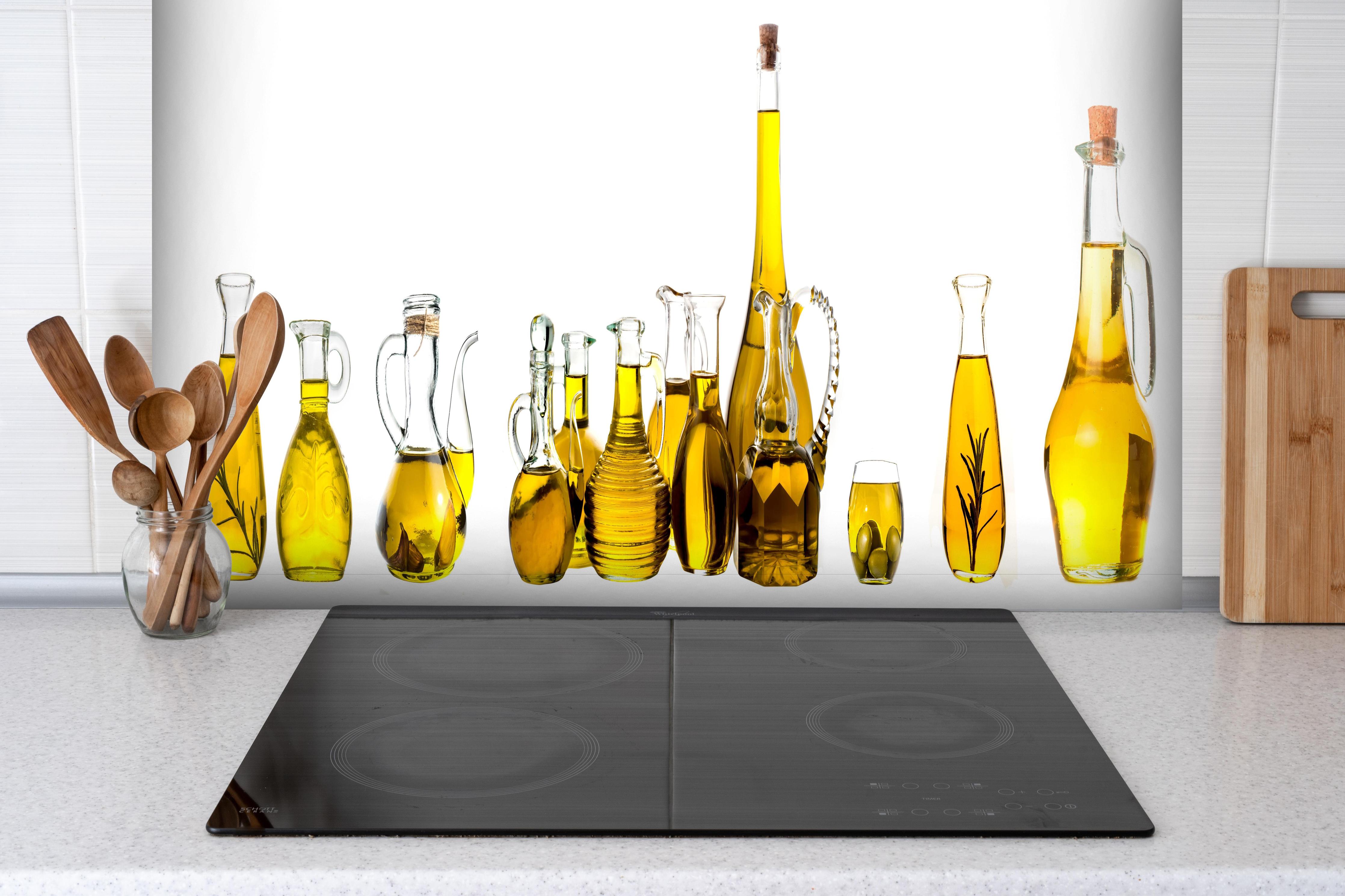 Spritzschutz - Elegante Auswahl Gelber Olivenölflaschen hinter einem Cerankochfeld zwischen Holz-Kochutensilien