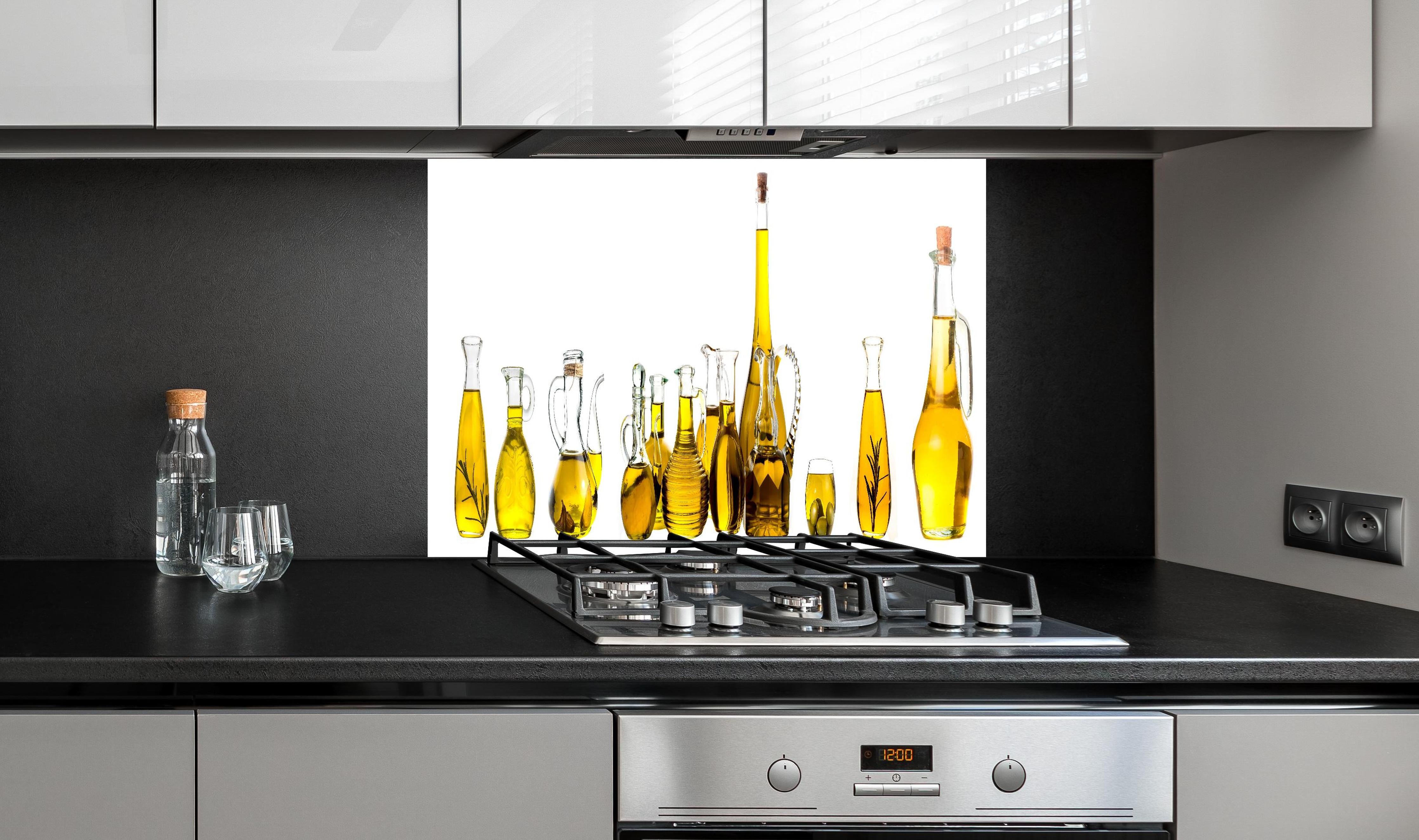 Spritzschutz - Elegante Auswahl Gelber Olivenölflaschen hinter einem Cerankochfeld zwischen Holz-Kochutensilien