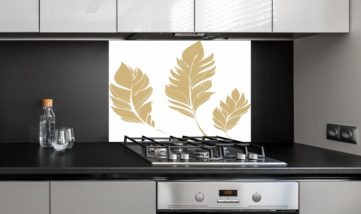 Spritzschutz - Elegante Goldfarbene Feder-Formen Set hinter einem Cerankochfeld zwischen Holz-Kochutensilien