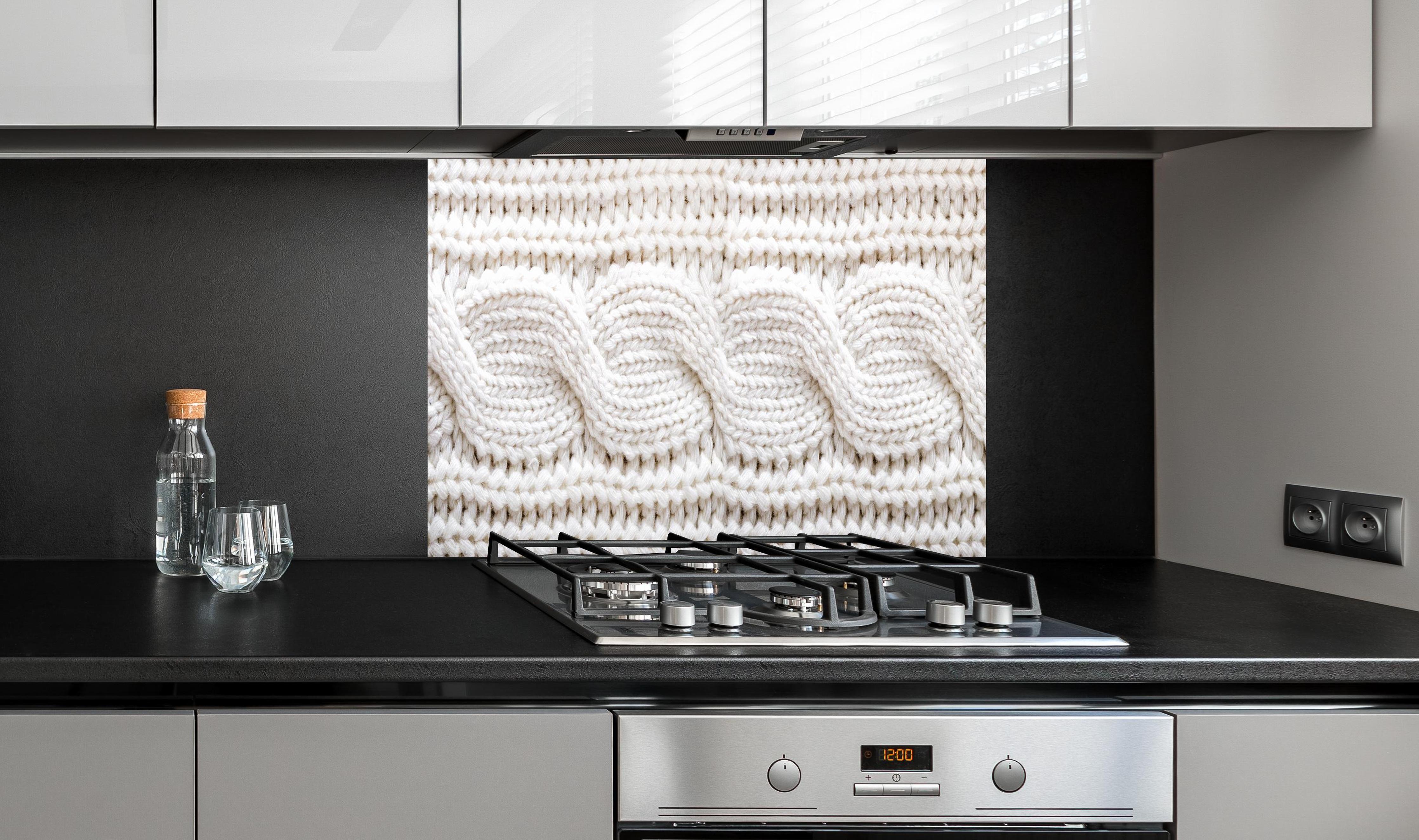 Spritzschutz - Elegante weiße Stricktextur aus Wolle hinter einem Cerankochfeld zwischen Holz-Kochutensilien