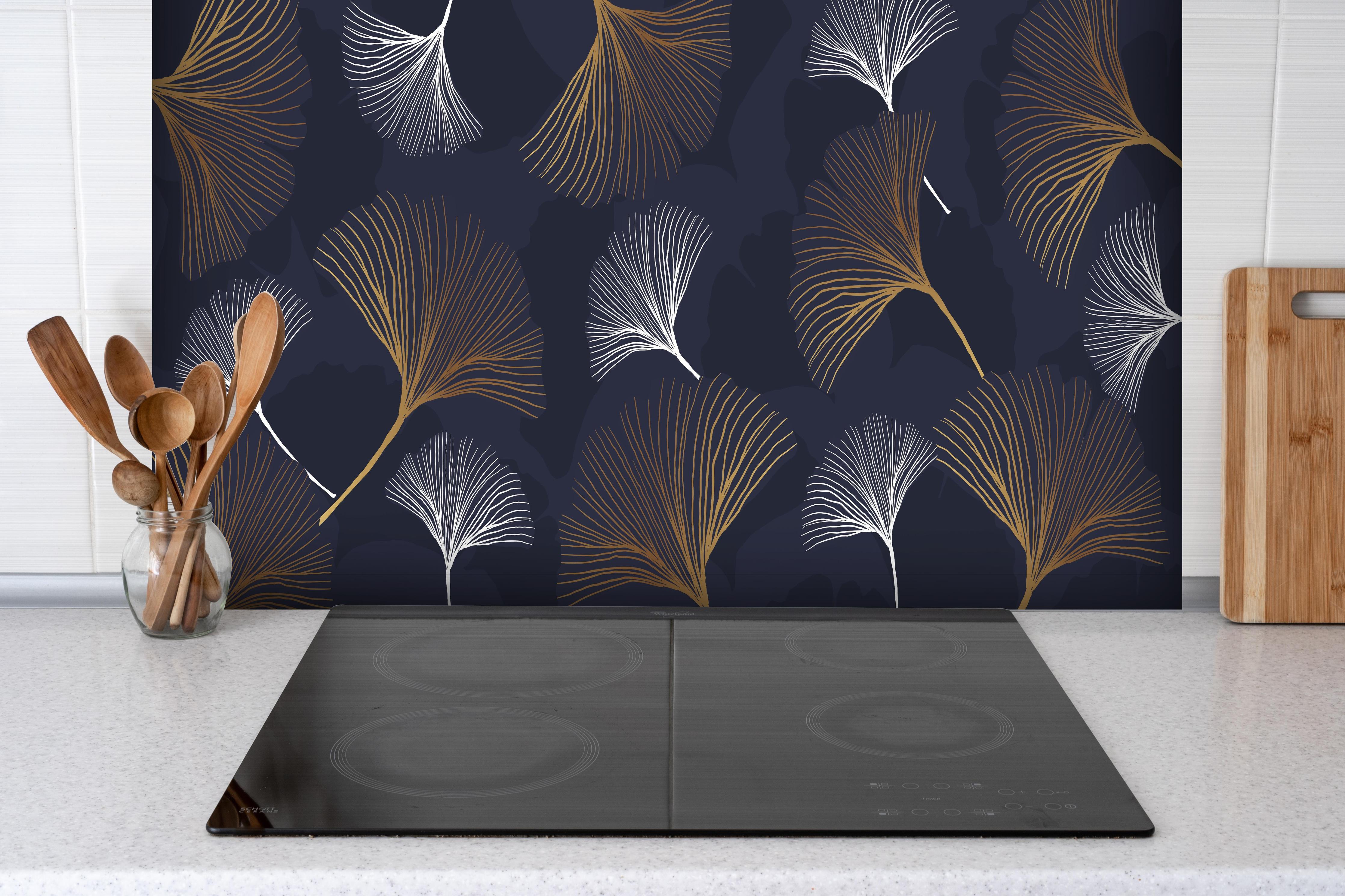 Spritzschutz - Eleganter metallischer Farn auf dunklem Hintergrund hinter einem Cerankochfeld zwischen Holz-Kochutensilien