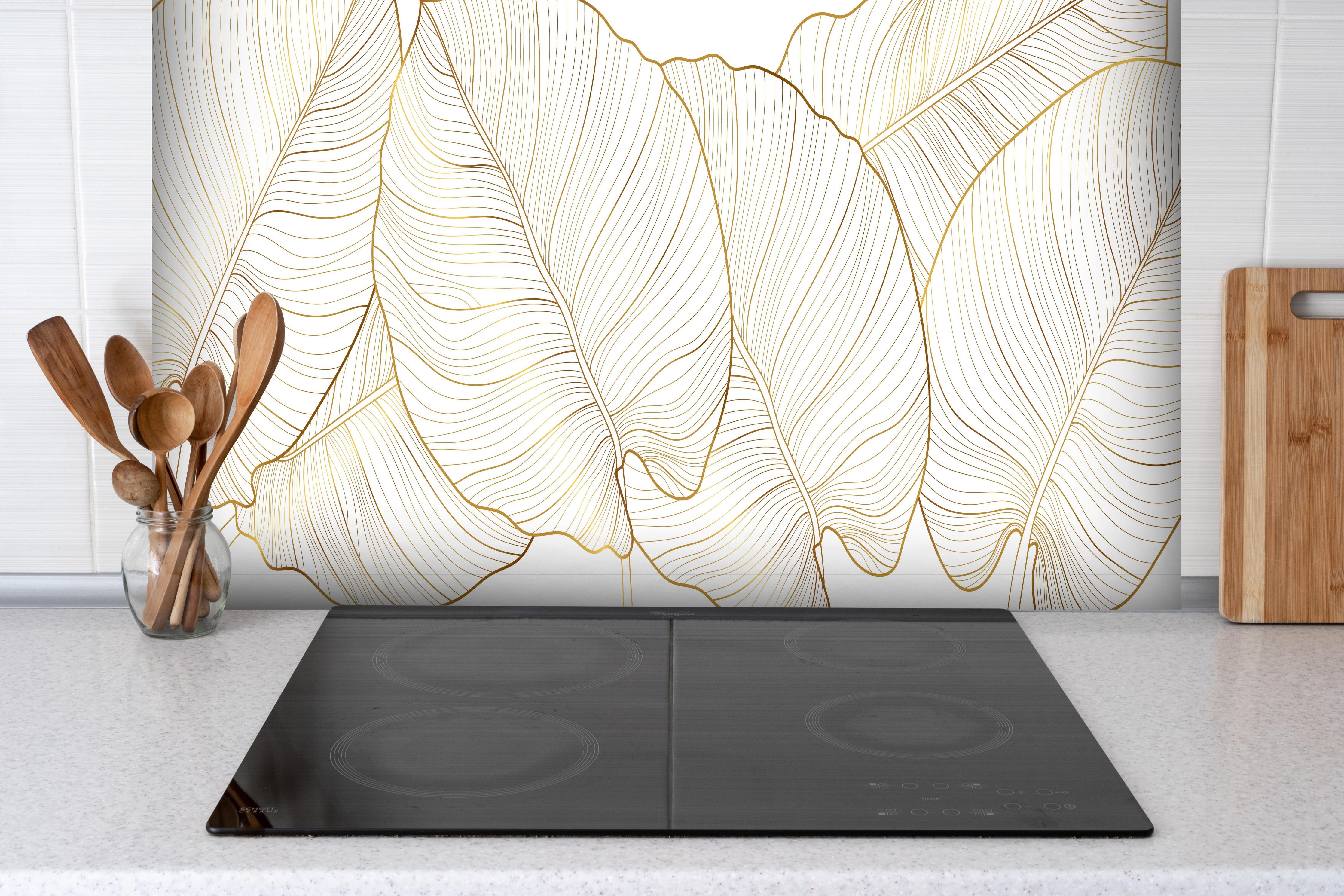 Spritzschutz - Elegantes Blatt-Design in Gold und Weiß hinter einem Cerankochfeld zwischen Holz-Kochutensilien