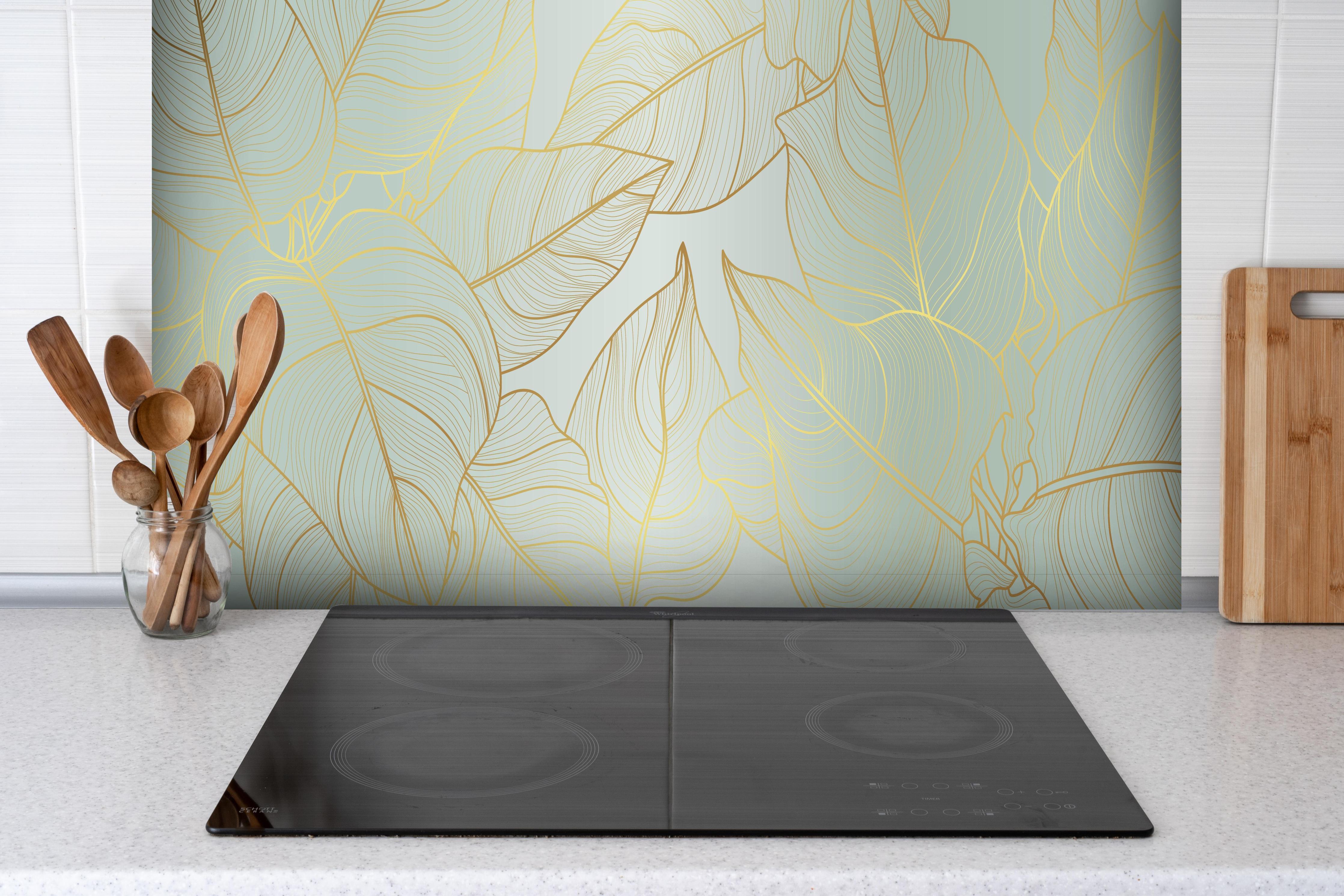 Spritzschutz - Elegantes Laub Design in Gold-Beige hinter einem Cerankochfeld zwischen Holz-Kochutensilien