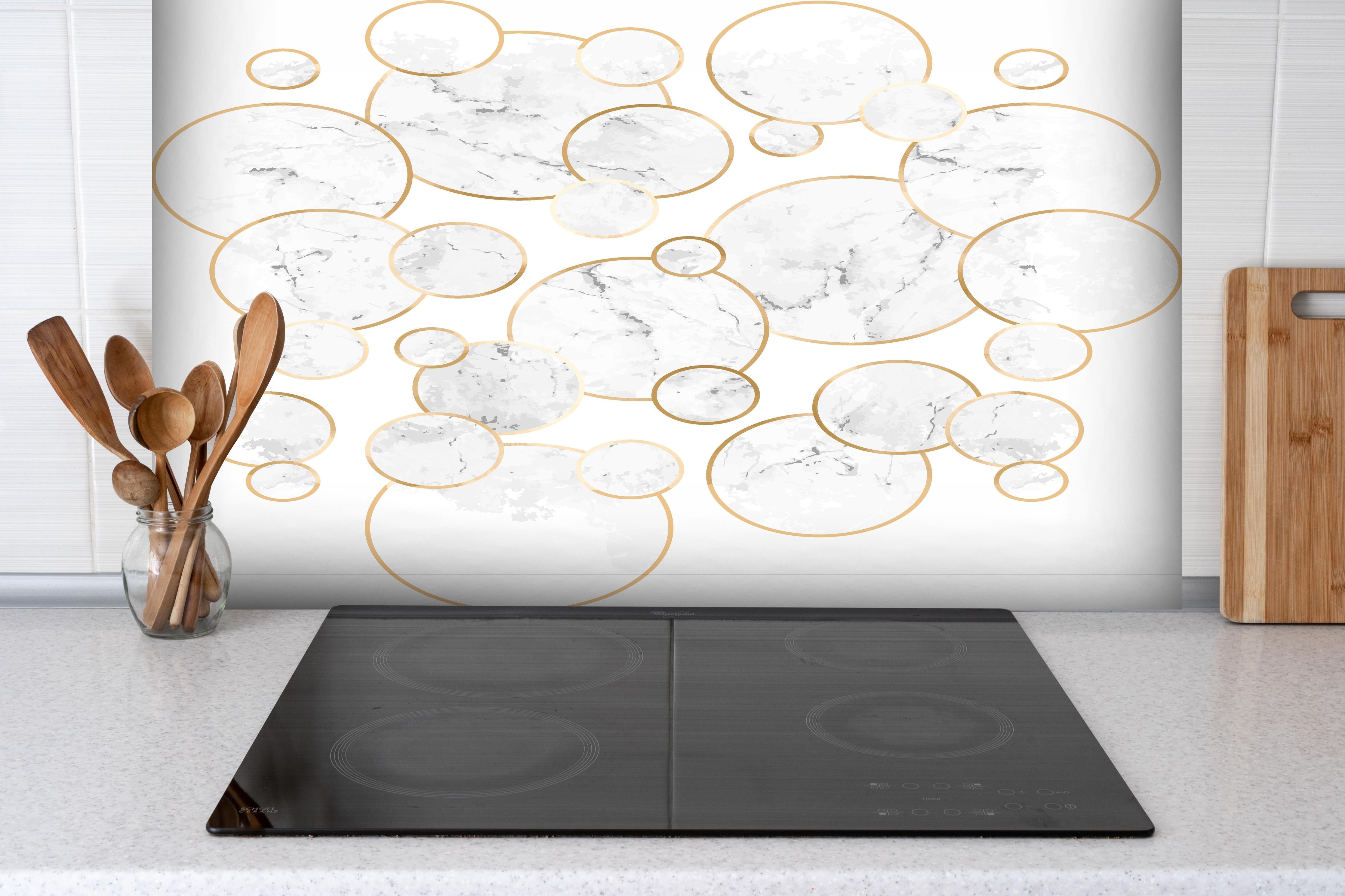 Spritzschutz - Elegantes Marmorkreis-Muster in Weiß-Gold hinter einem Cerankochfeld zwischen Holz-Kochutensilien