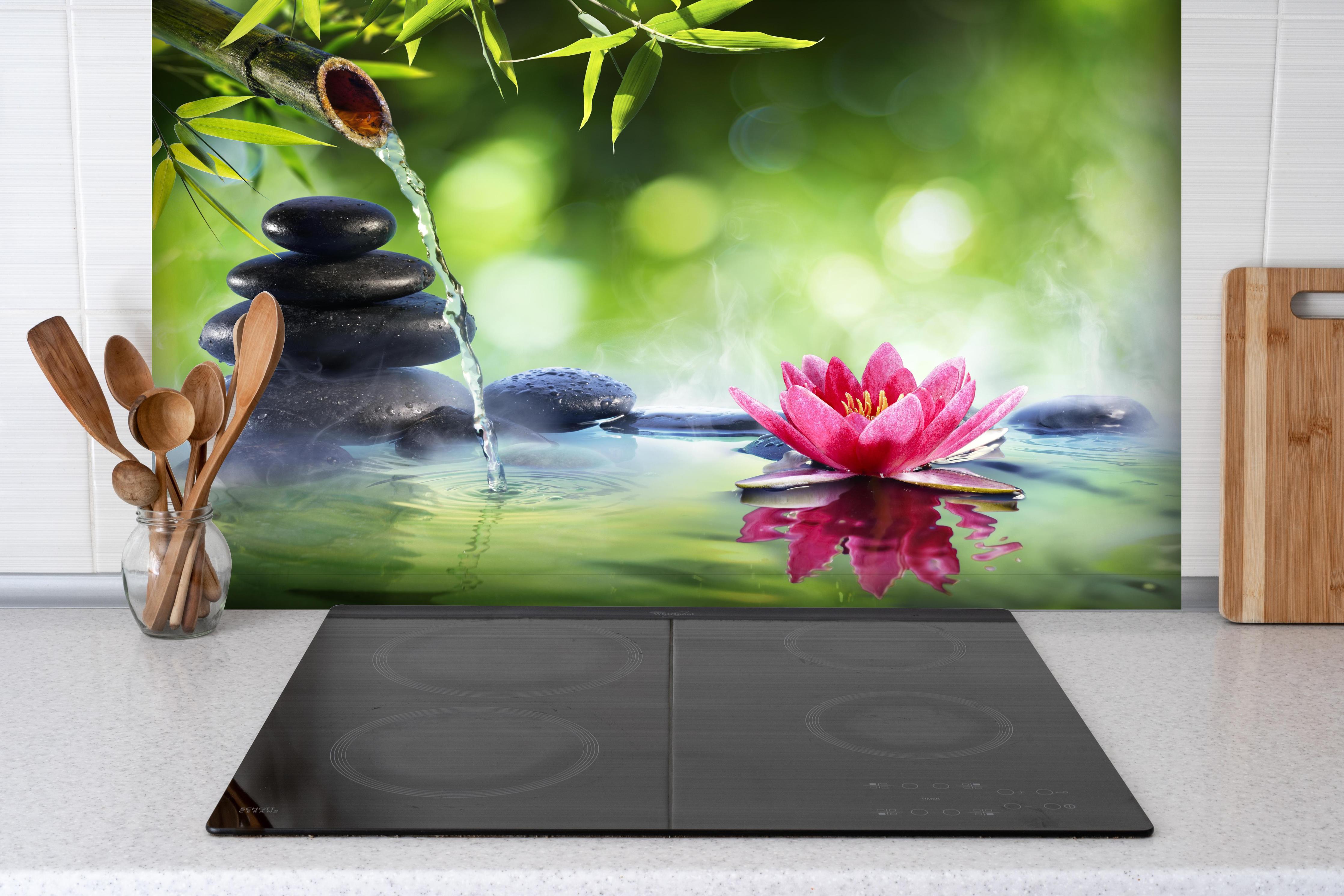 Spritzschutz - Entspannende Zen-Steine und pinkfarbene Lotusblüte hinter einem Cerankochfeld zwischen Holz-Kochutensilien