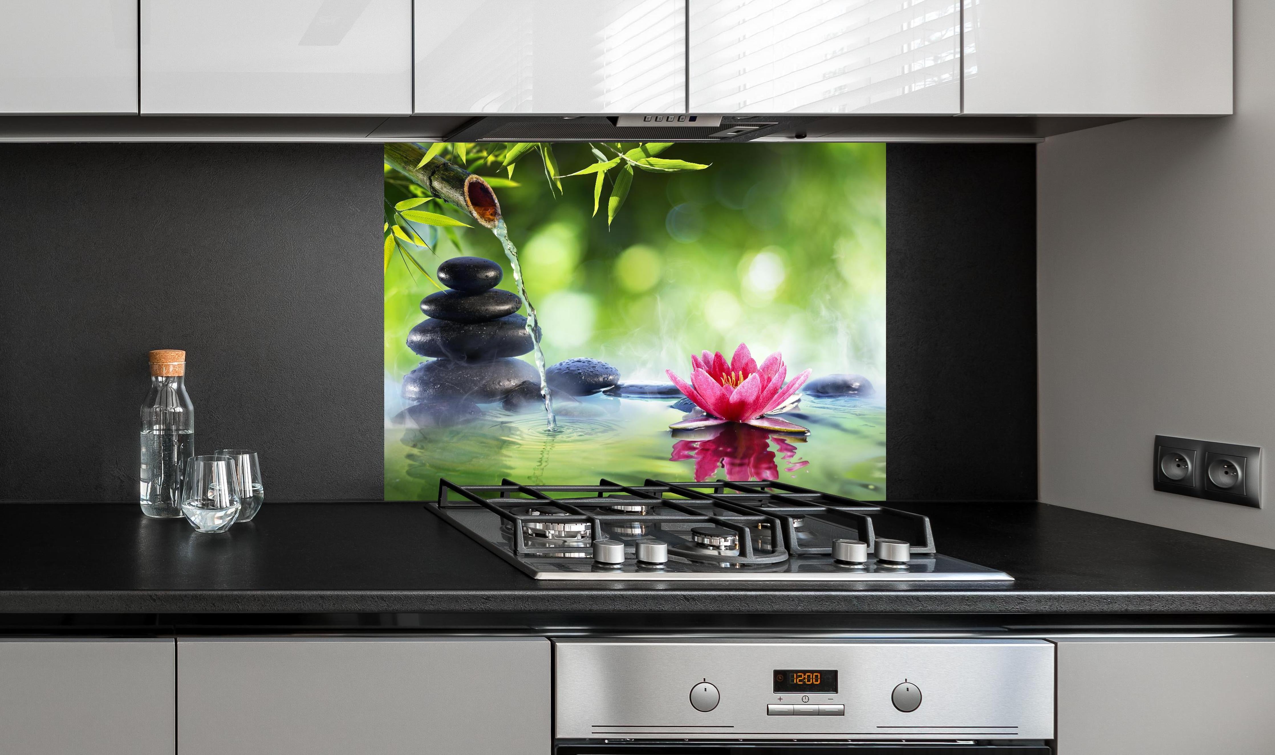 Spritzschutz - Entspannende Zen-Steine und pinkfarbene Lotusblüte hinter einem Cerankochfeld zwischen Holz-Kochutensilien