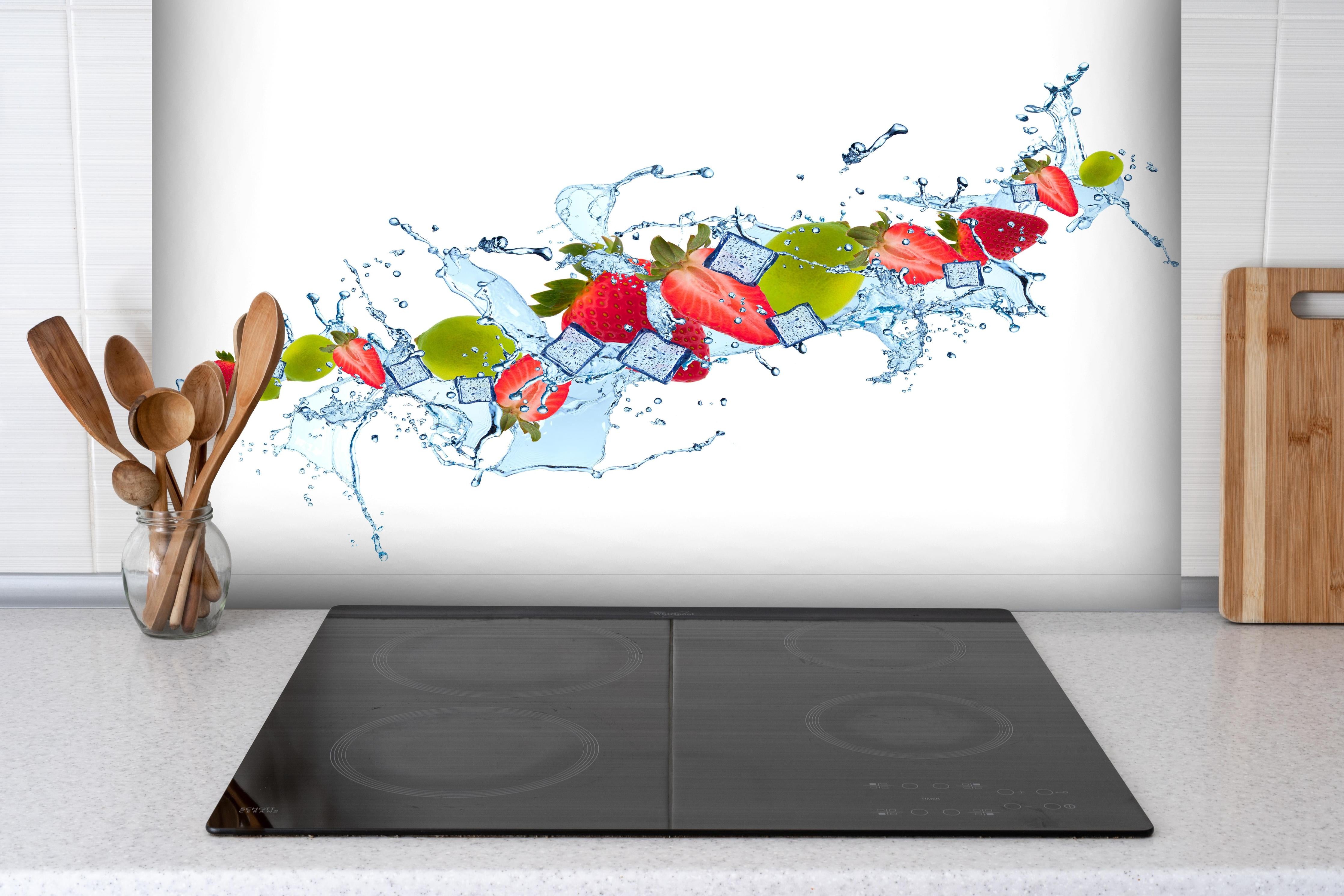 Spritzschutz - Erfrischende Wasserspritzer mit Erdbeere und Limette hinter einem Cerankochfeld zwischen Holz-Kochutensilien