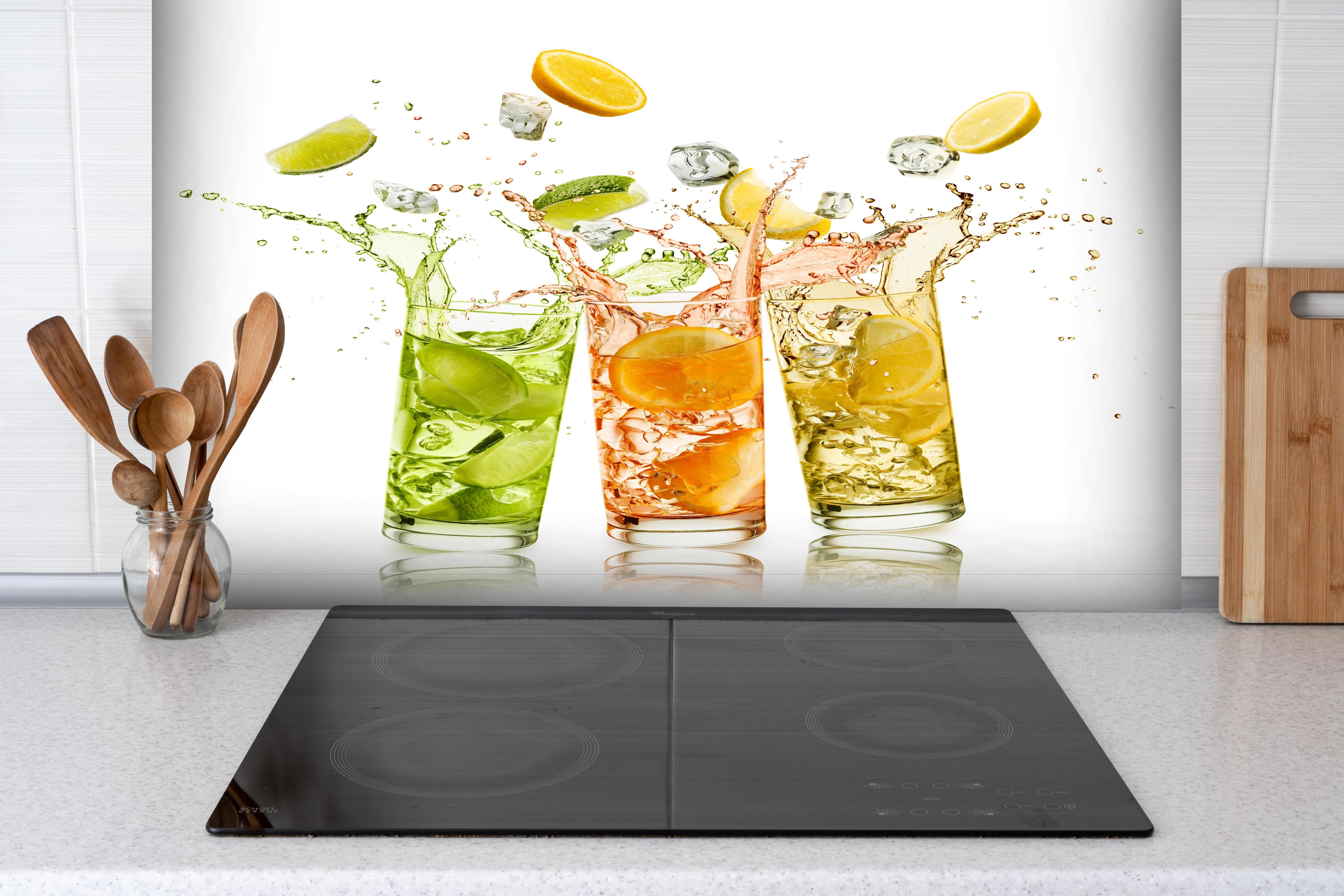 Spritzschutz - Erfrischungsgetränke mit Zitrusfrüchten hinter einem Cerankochfeld zwischen Holz-Kochutensilien