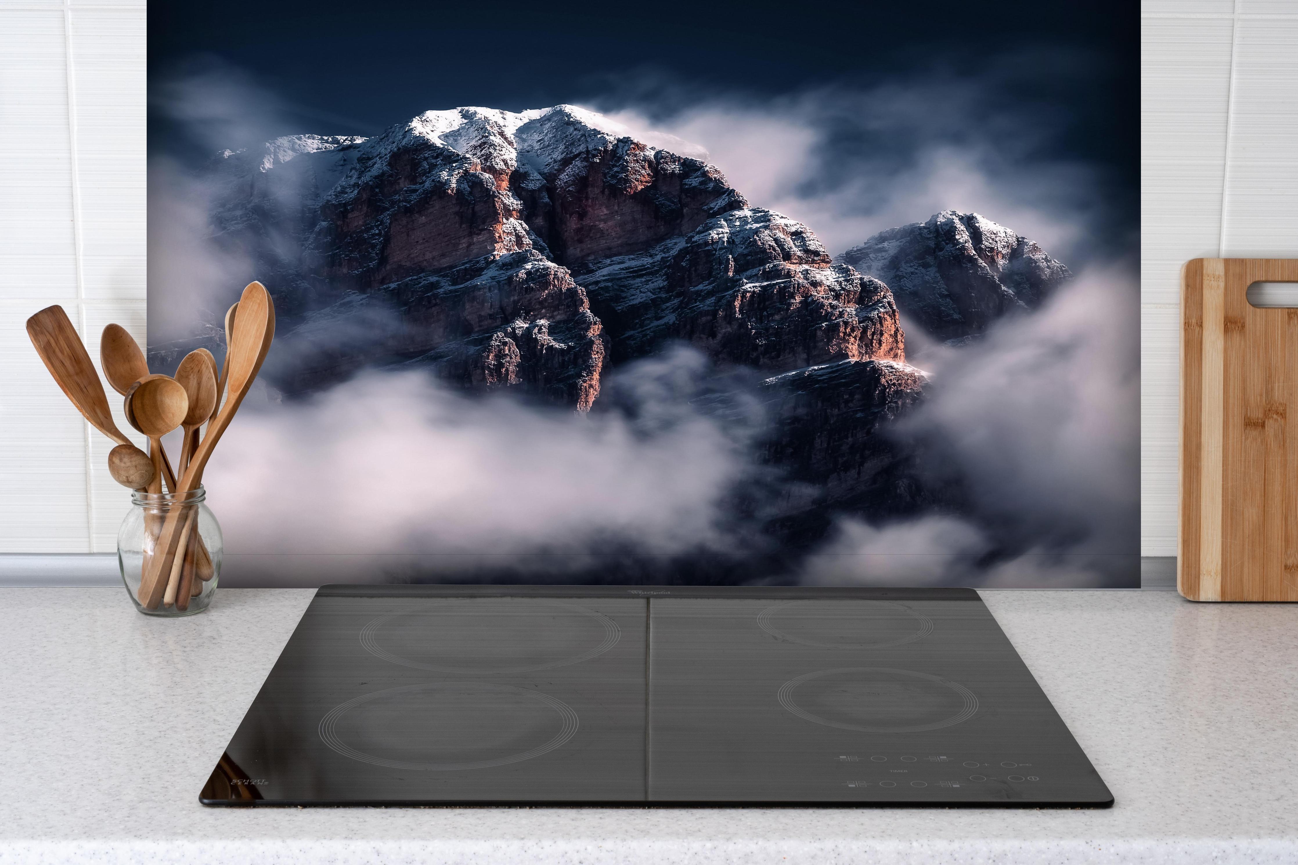 Spritzschutz - Erhabene Winterberge in Nebel und Schnee hinter einem Cerankochfeld zwischen Holz-Kochutensilien