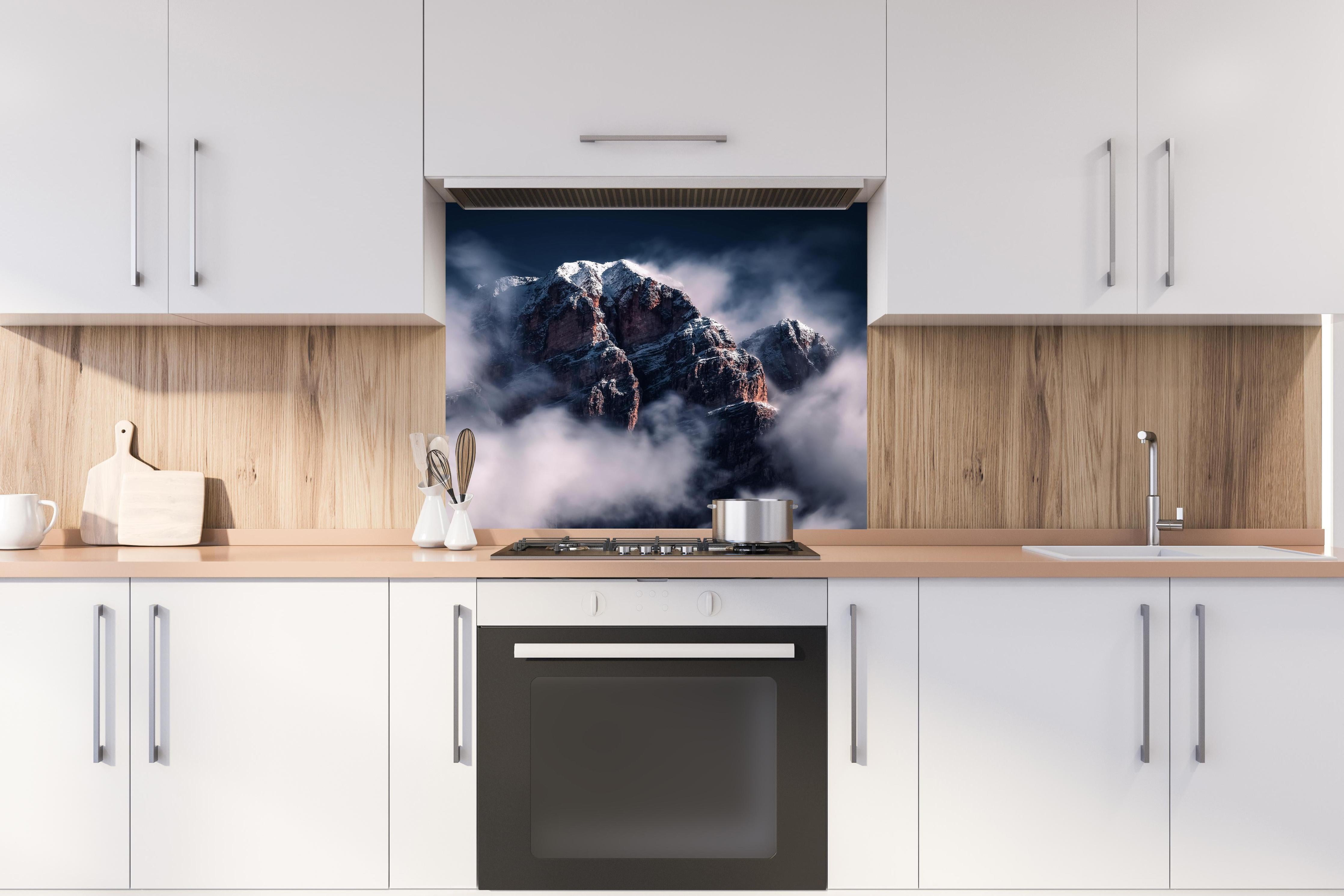 Spritzschutz - Erhabene Winterberge in Nebel und Schnee hinter einem Cerankochfeld zwischen Holz-Kochutensilien