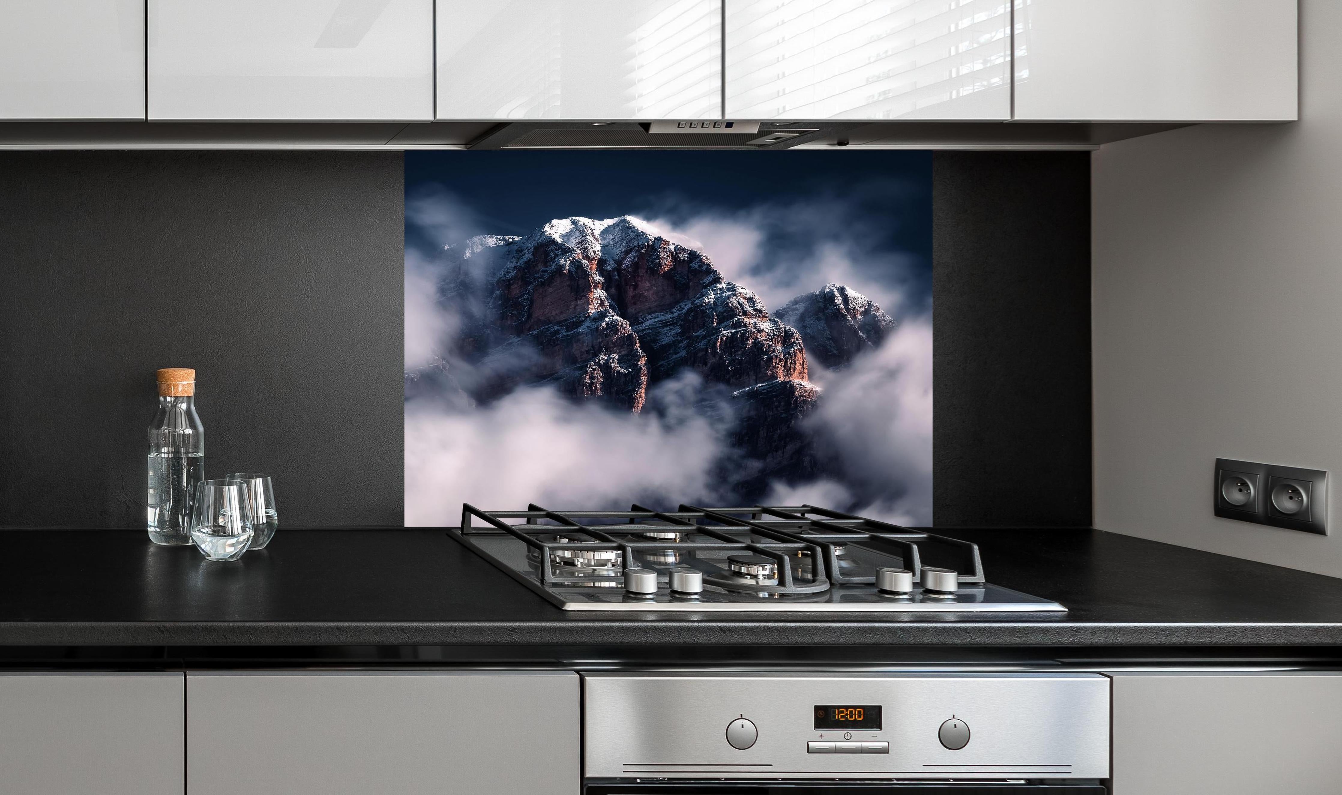 Spritzschutz - Erhabene Winterberge in Nebel und Schnee hinter einem Cerankochfeld zwischen Holz-Kochutensilien