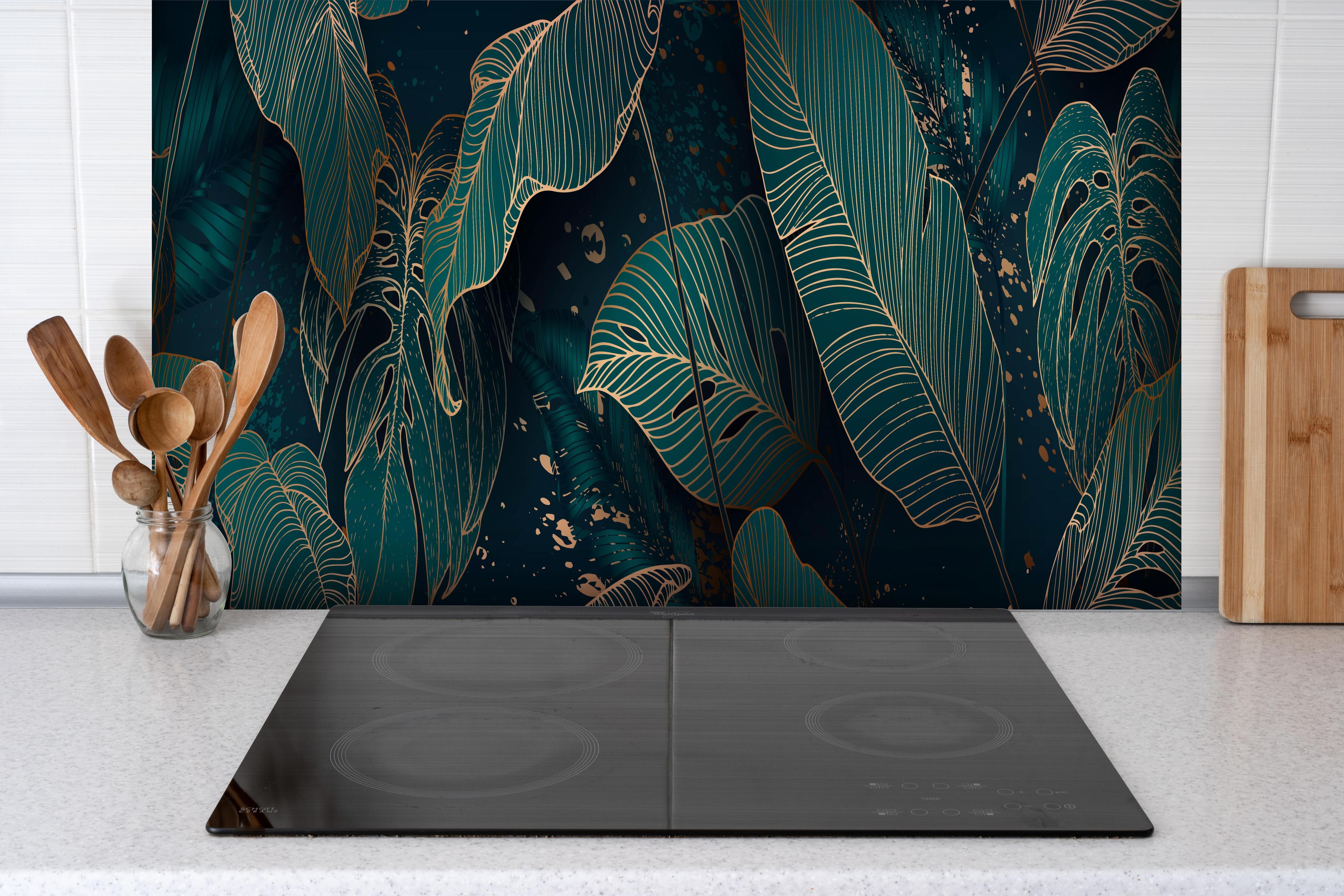 Spritzschutz - Exotische Dunkelgrüne Blätter mit Gold hinter einem Cerankochfeld zwischen Holz-Kochutensilien