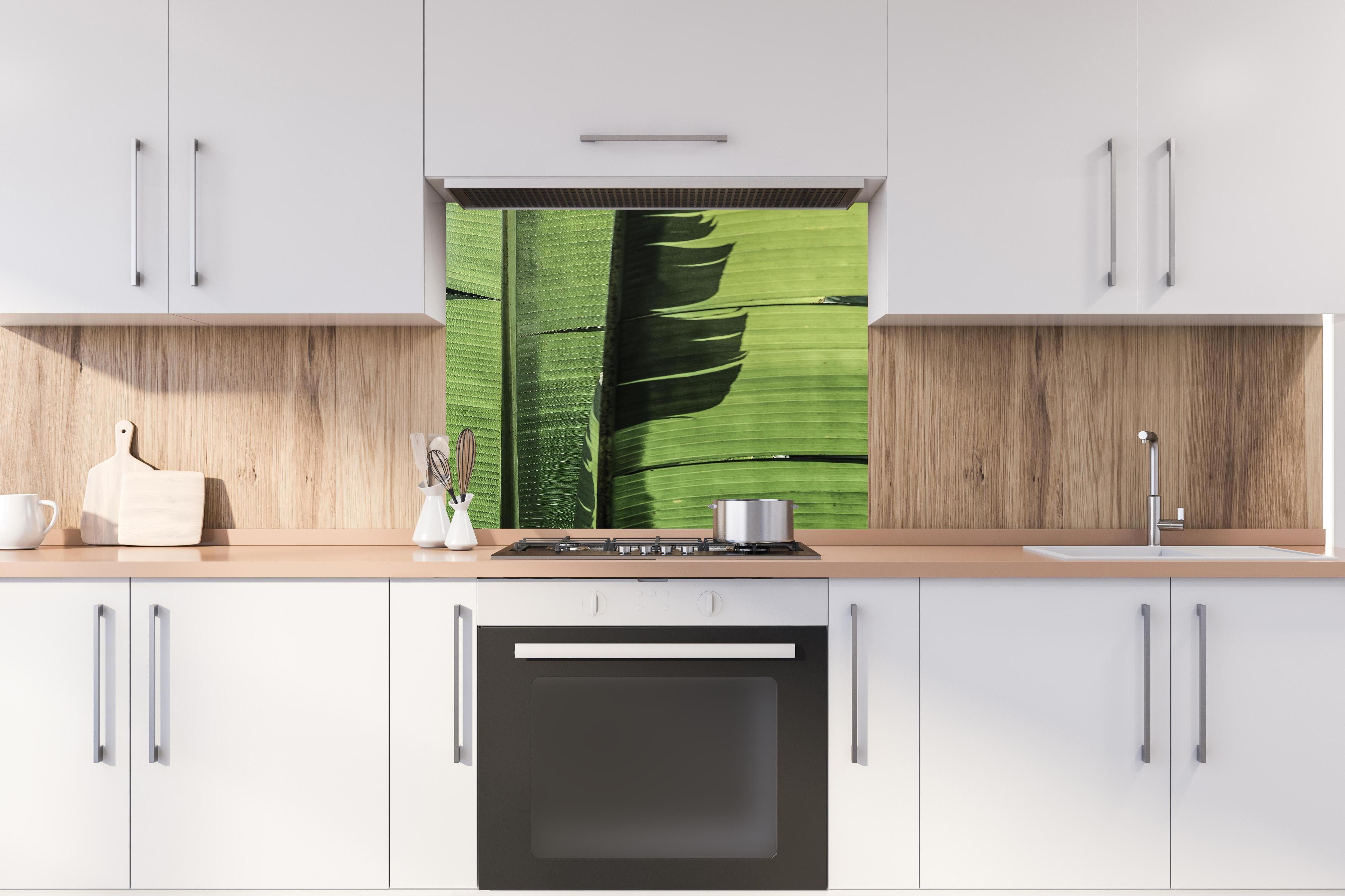 Spritzschutz - Exotisches grünes Palmenblatt-Design hinter einem Cerankochfeld zwischen Holz-Kochutensilien