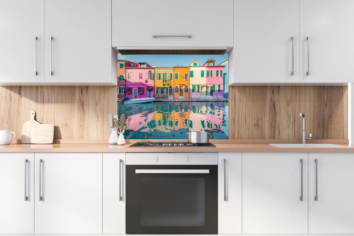 Spritzschutz - Farbenfrohe Häuser am Wasser in Burano, Venedig hinter einem Cerankochfeld zwischen Holz-Kochutensilien