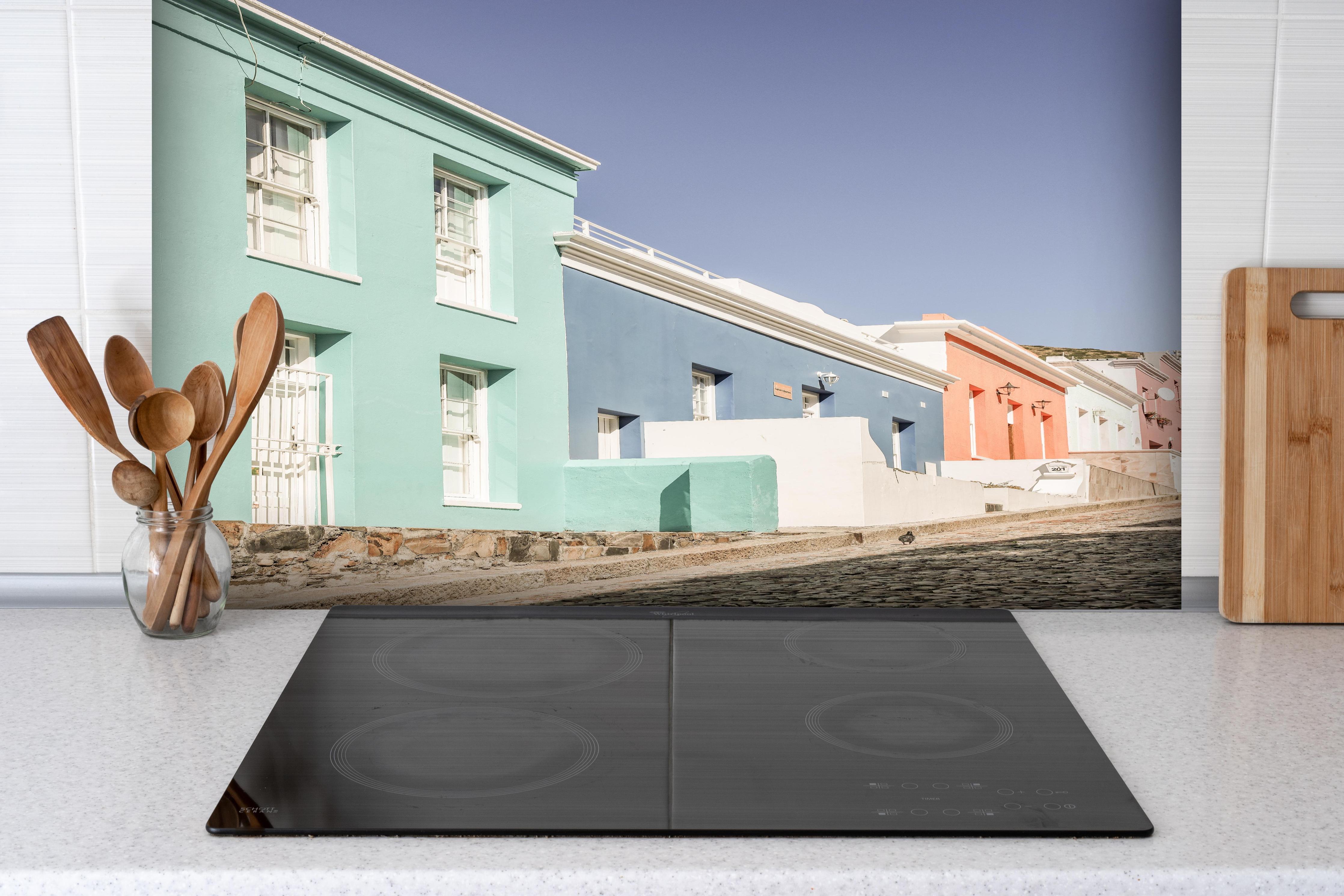 Spritzschutz - Farbenfrohe Hausfassaden unter klarem Himmel hinter einem Cerankochfeld zwischen Holz-Kochutensilien