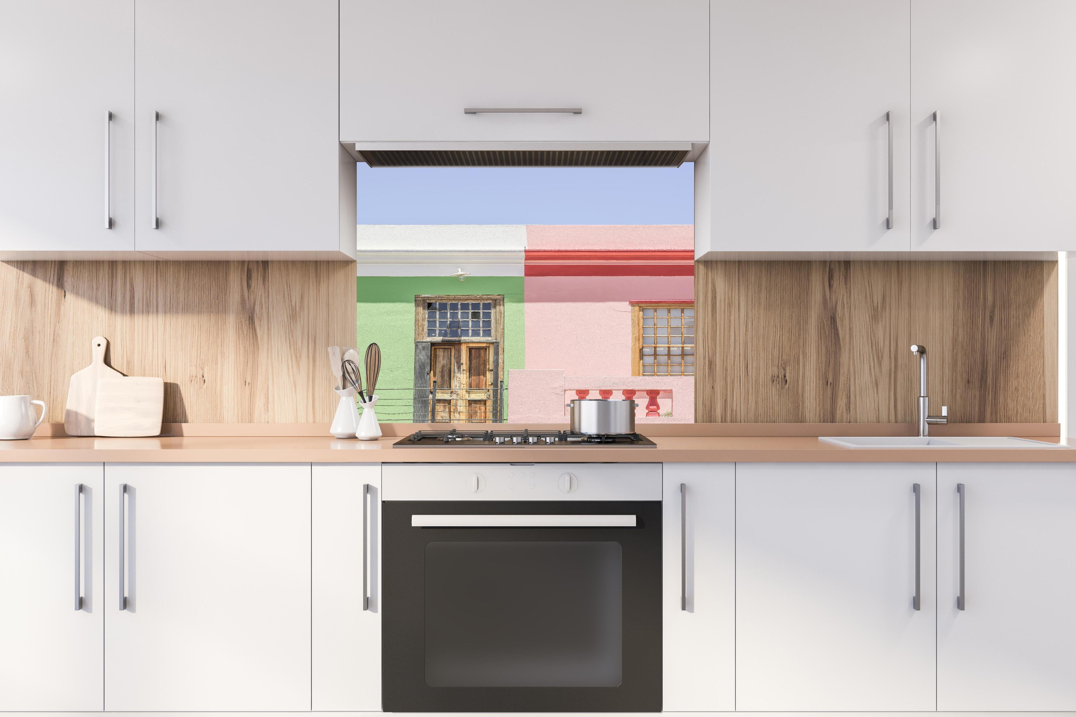 Spritzschutz - Farbenfrohe Stadthaus Fassaden im Sonnenlicht hinter einem Cerankochfeld zwischen Holz-Kochutensilien