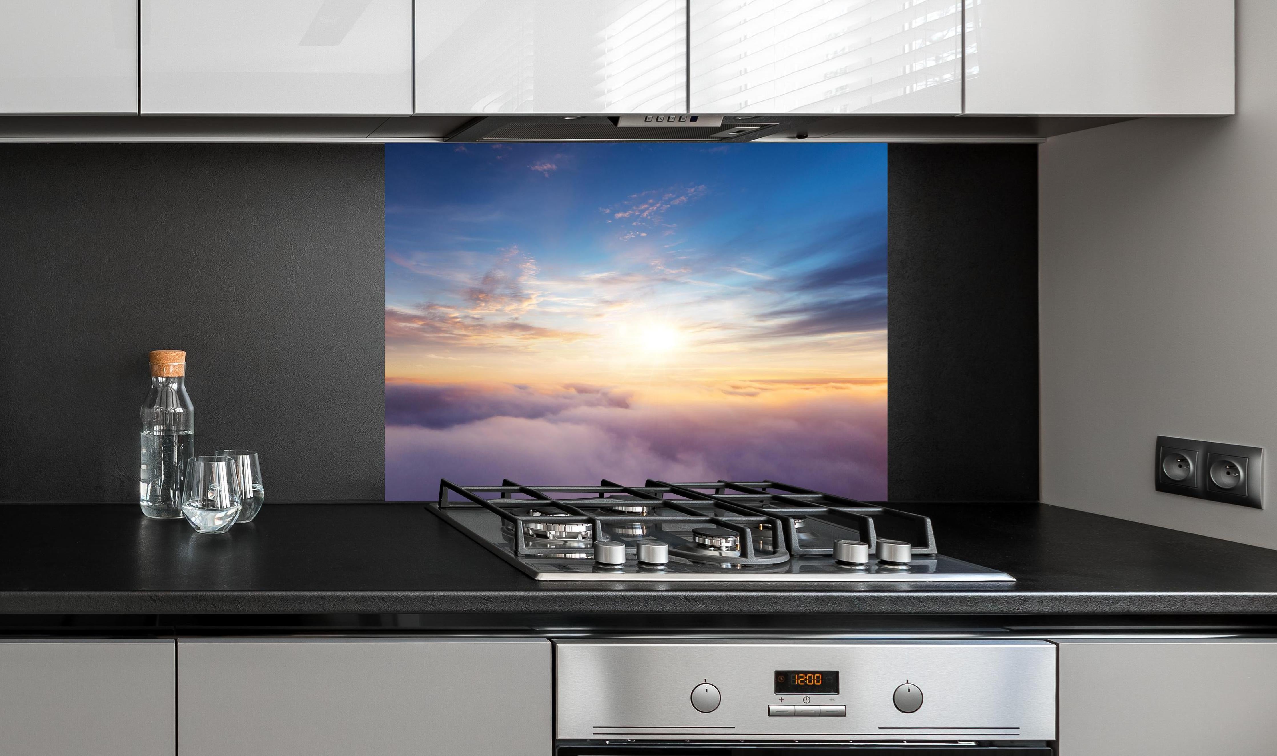 Spritzschutz - Farbenfrohe Wolken bei Sonnenaufgang hinter einem Cerankochfeld zwischen Holz-Kochutensilien