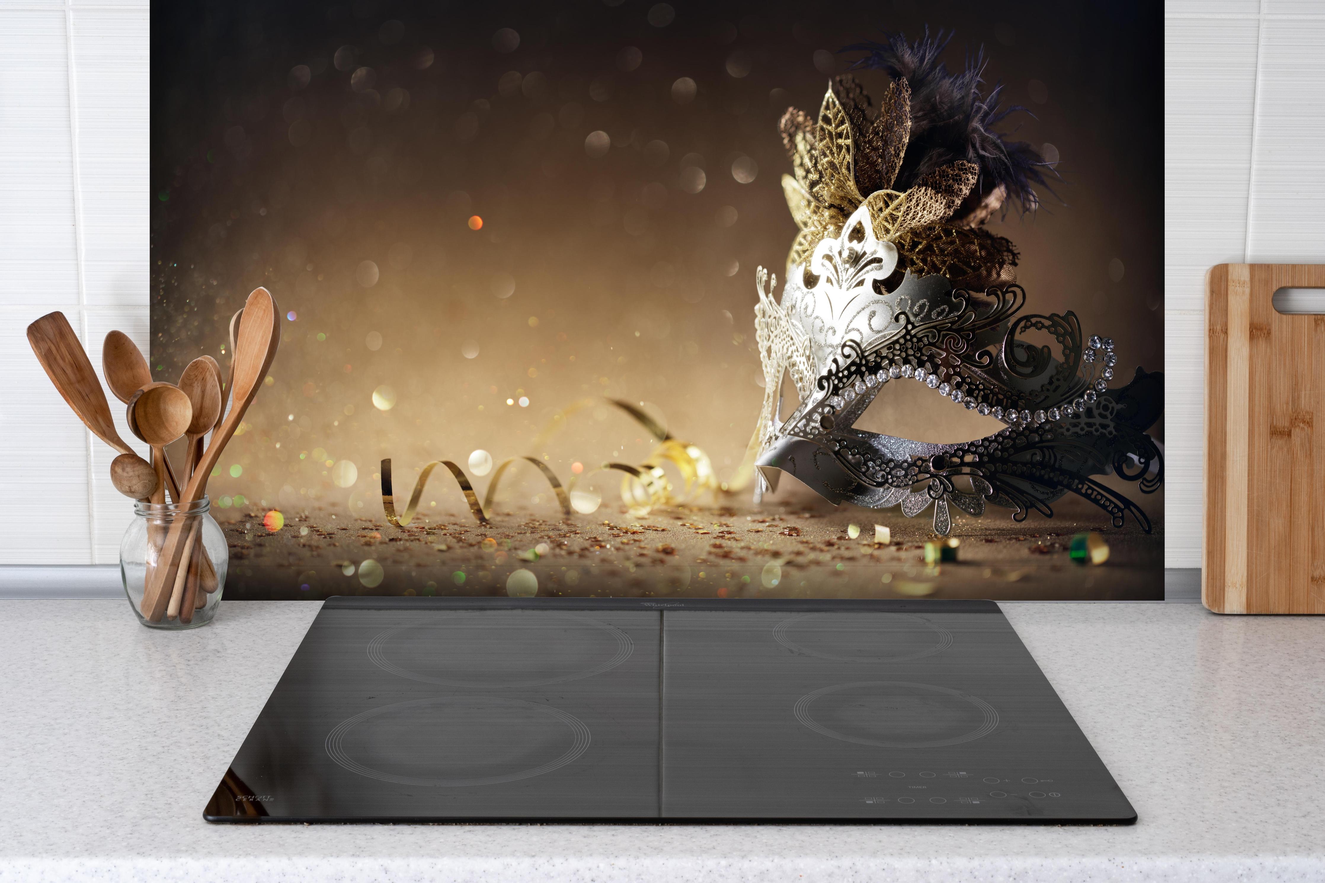 Spritzschutz - Faschingsmaske mit Glitter hinter einem Cerankochfeld zwischen Holz-Kochutensilien