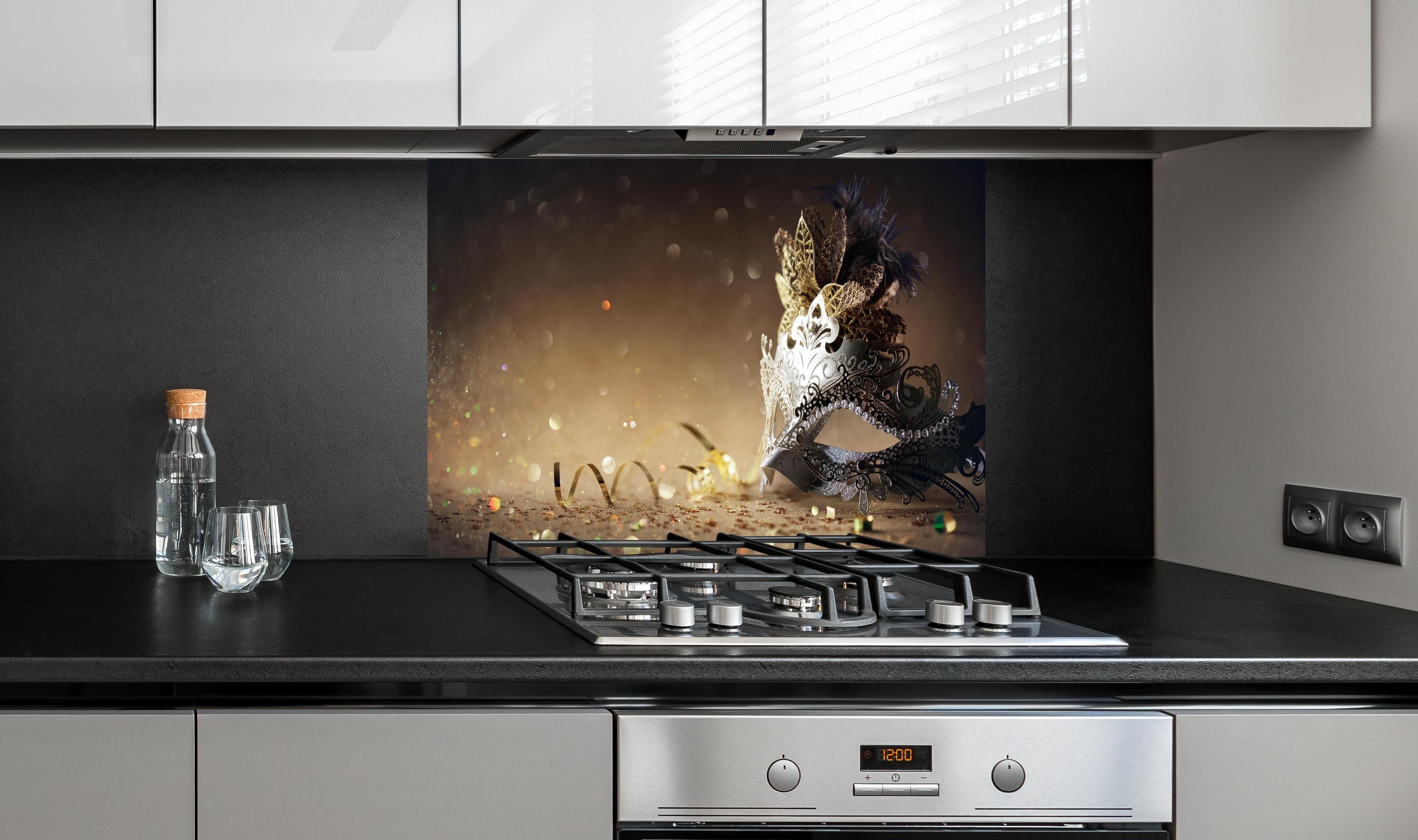 Spritzschutz - Faschingsmaske mit Glitter hinter einem Cerankochfeld zwischen Holz-Kochutensilien