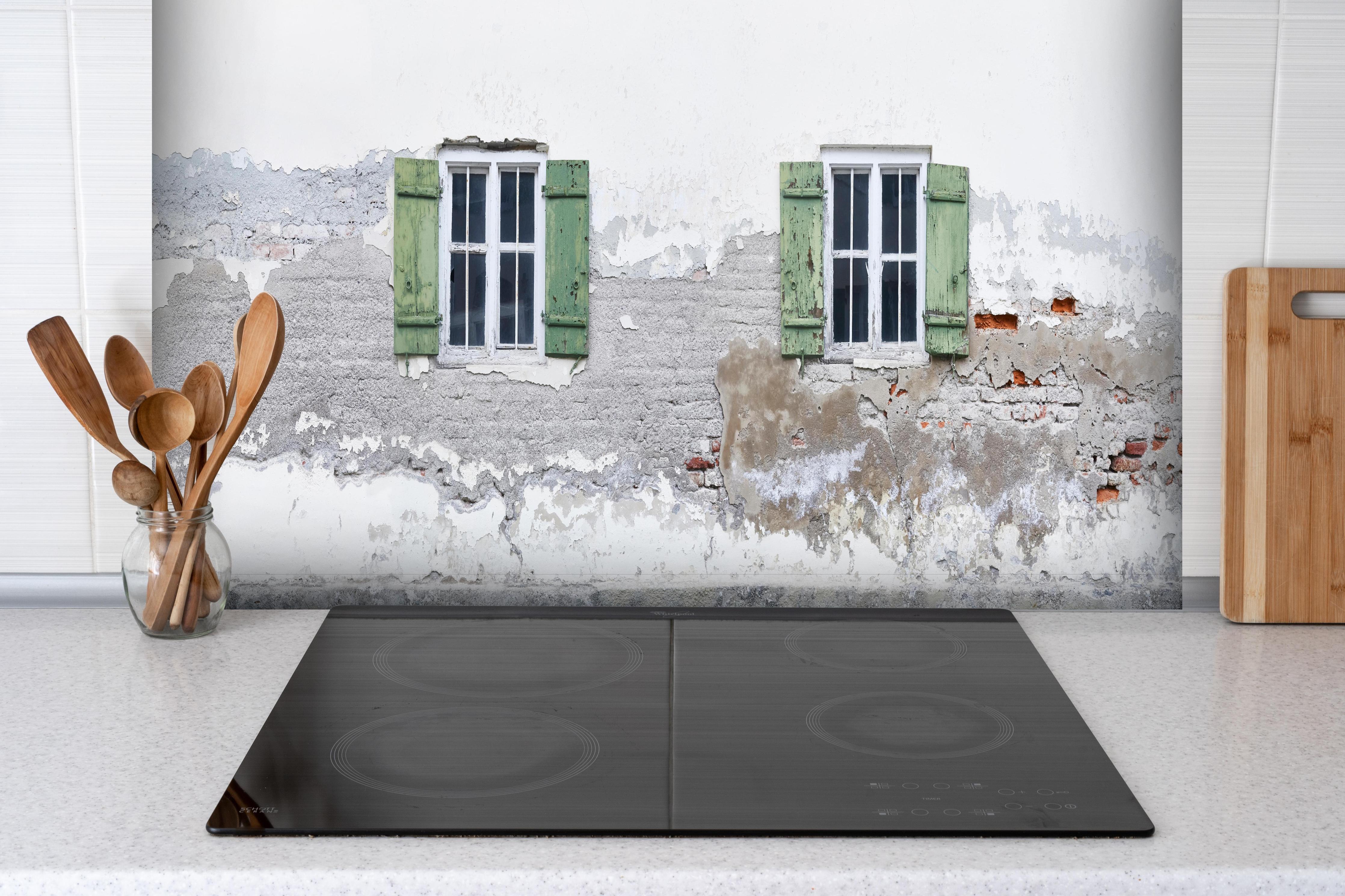 Spritzschutz - Fensterrahmen einer veralteten Hauswand hinter einem Cerankochfeld zwischen Holz-Kochutensilien
